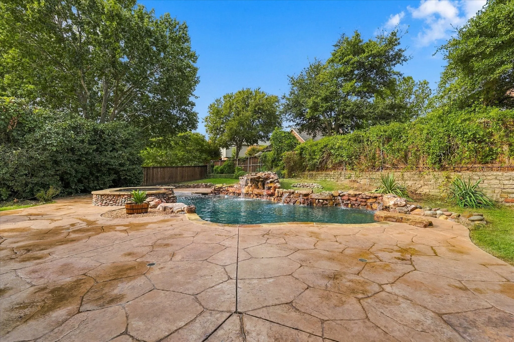Outdoor oasis featuring a flagstone patio, natural rock-accented pool, integrated stone waterfall, raised spa, and stone retaining wall