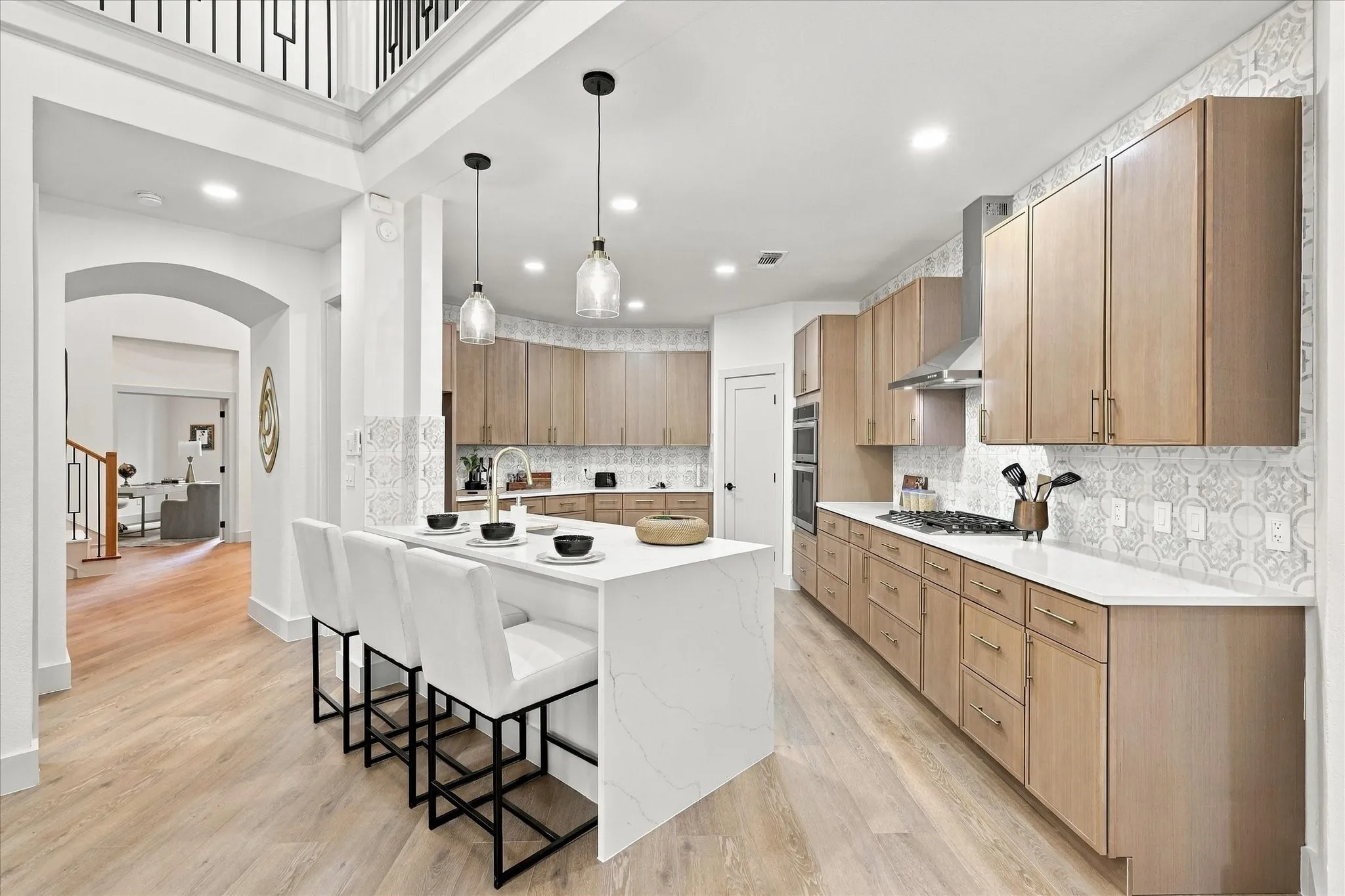 Kitchen featuring a large central island with a stone countertop, flat-panel wood cabinetry, patterned tile backsplash, stainless steel gas cooktop with range hood, and wood-finish flooring
