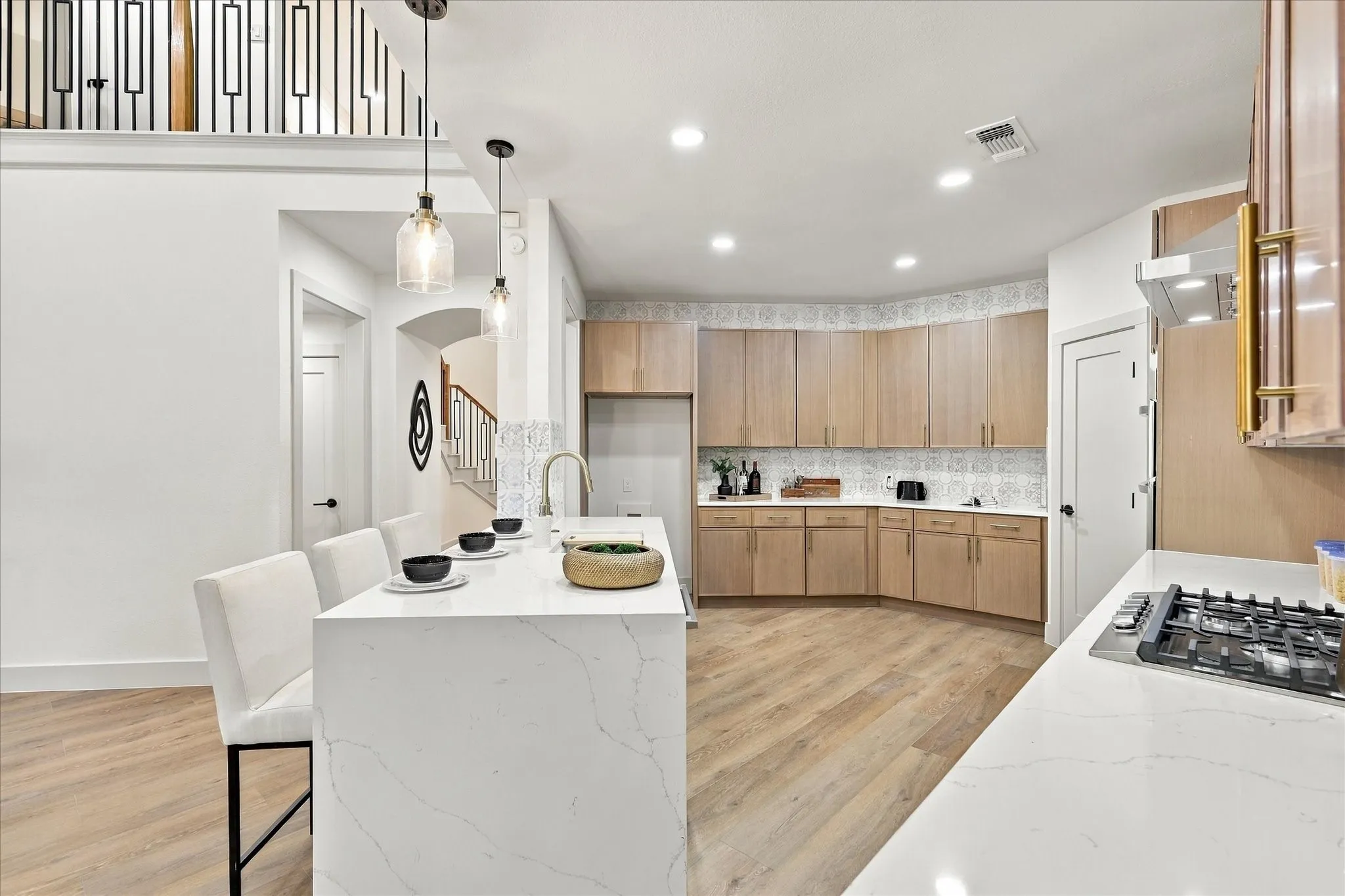Kitchen featuring a waterfall-edge island with stone-surface countertop, flat-panel light wood cabinetry, decorative patterned tile backsplash, recessed lighting, and wood-finish flooring
