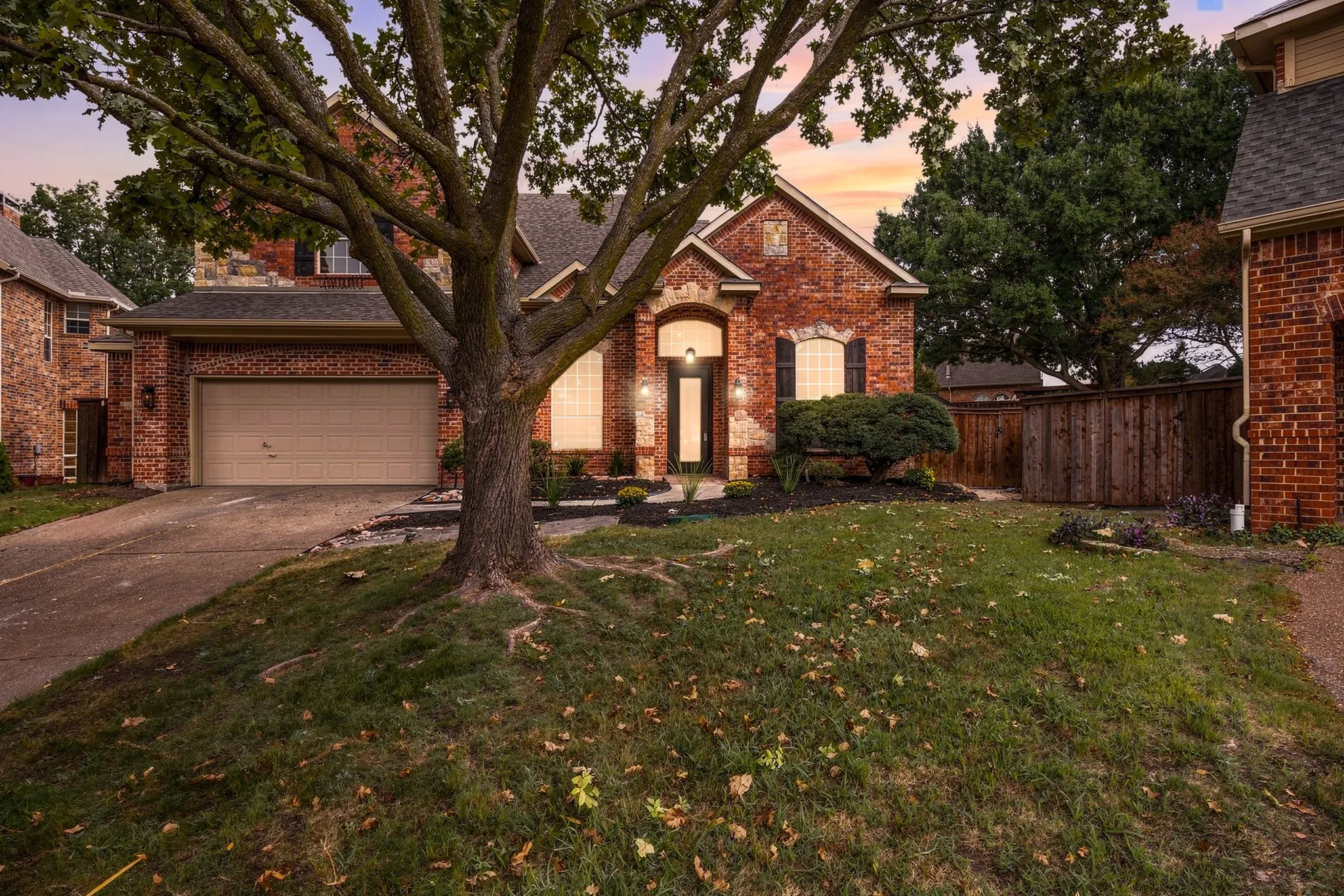 Traditional brick exterior featuring an arched entryway, gabled rooflines, attached two-car garage, and mature tree landscaping