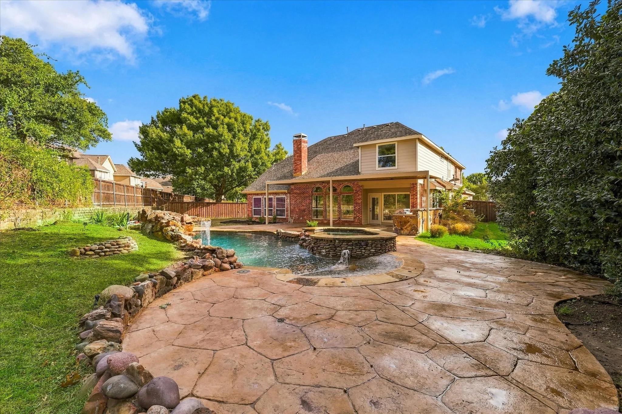 Backyard featuring an in-ground swimming pool with an integrated stone spa, stone water feature, decorative stamped concrete patio, and a covered rear porch