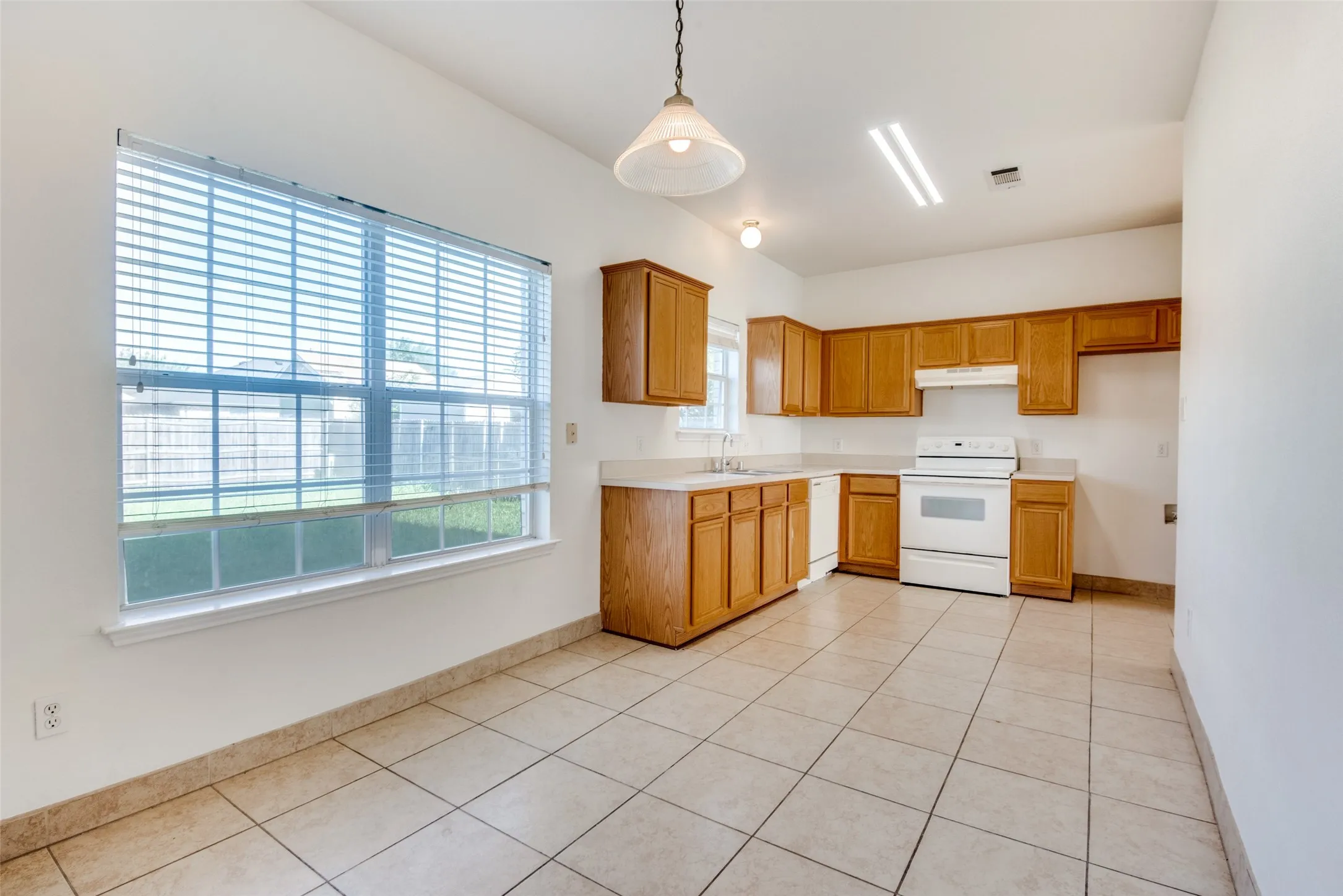 Kitchen featuring sink, hanging light fixtures, white appliances, and light tile patterned floors