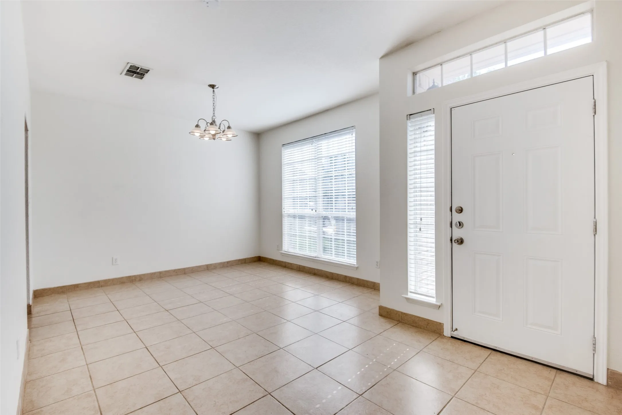 Tiled entryway with a notable chandelier