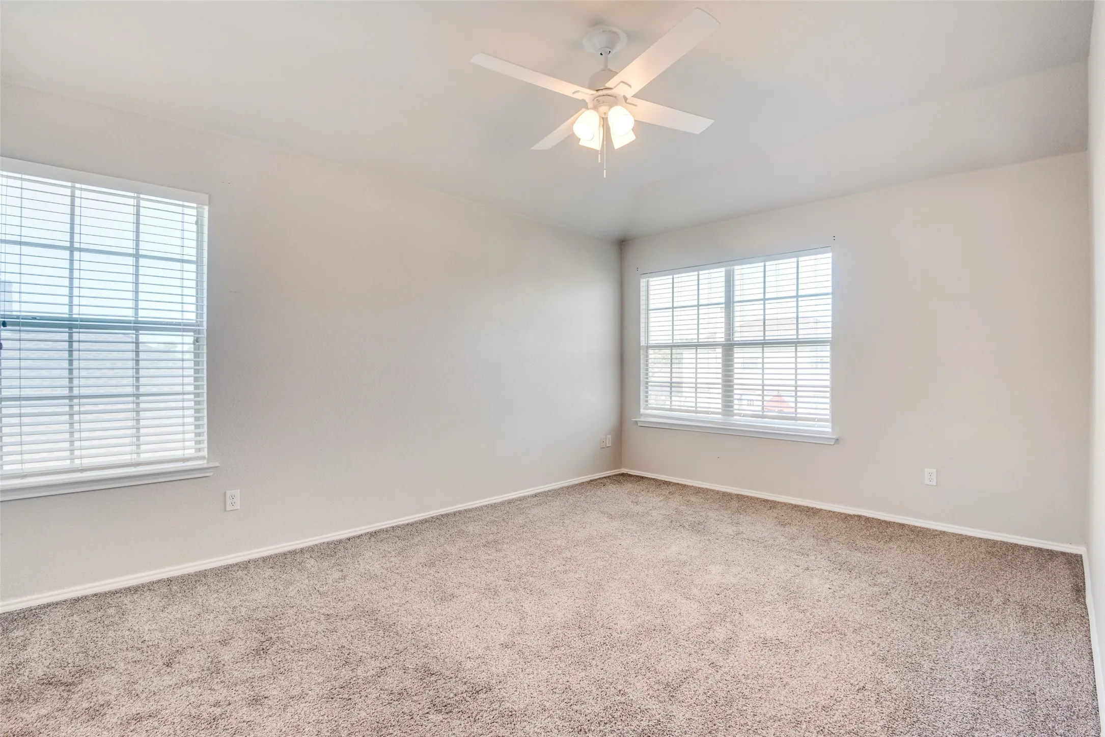Carpeted spare room featuring ceiling fan and a wealth of natural light