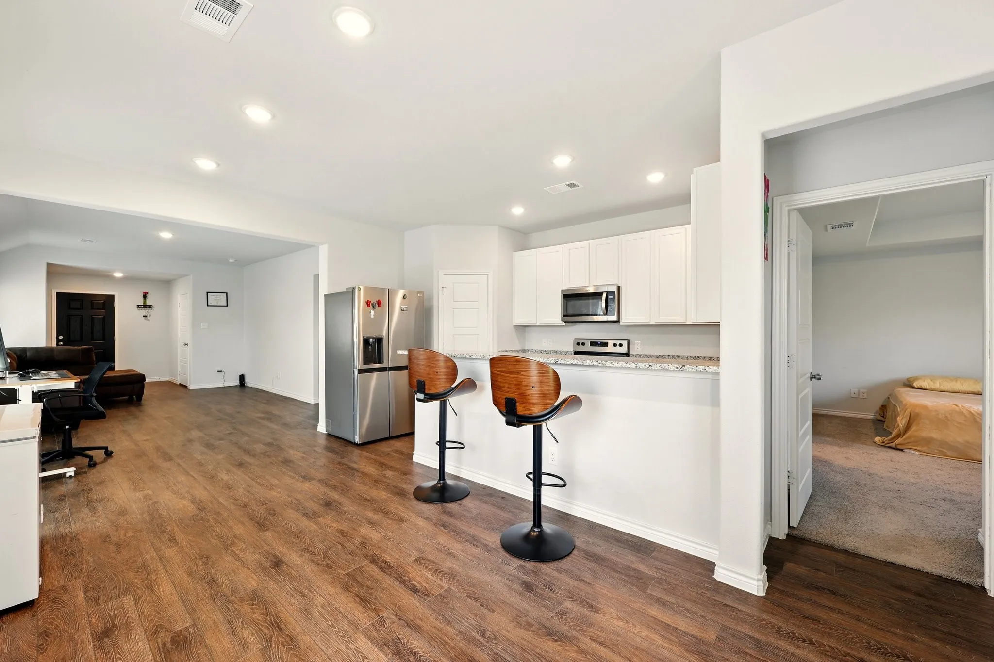 Spacious interior featuring wood-finish flooring, recessed lighting, white cabinetry, stainless steel appliances, and a kitchen island with stone countertops