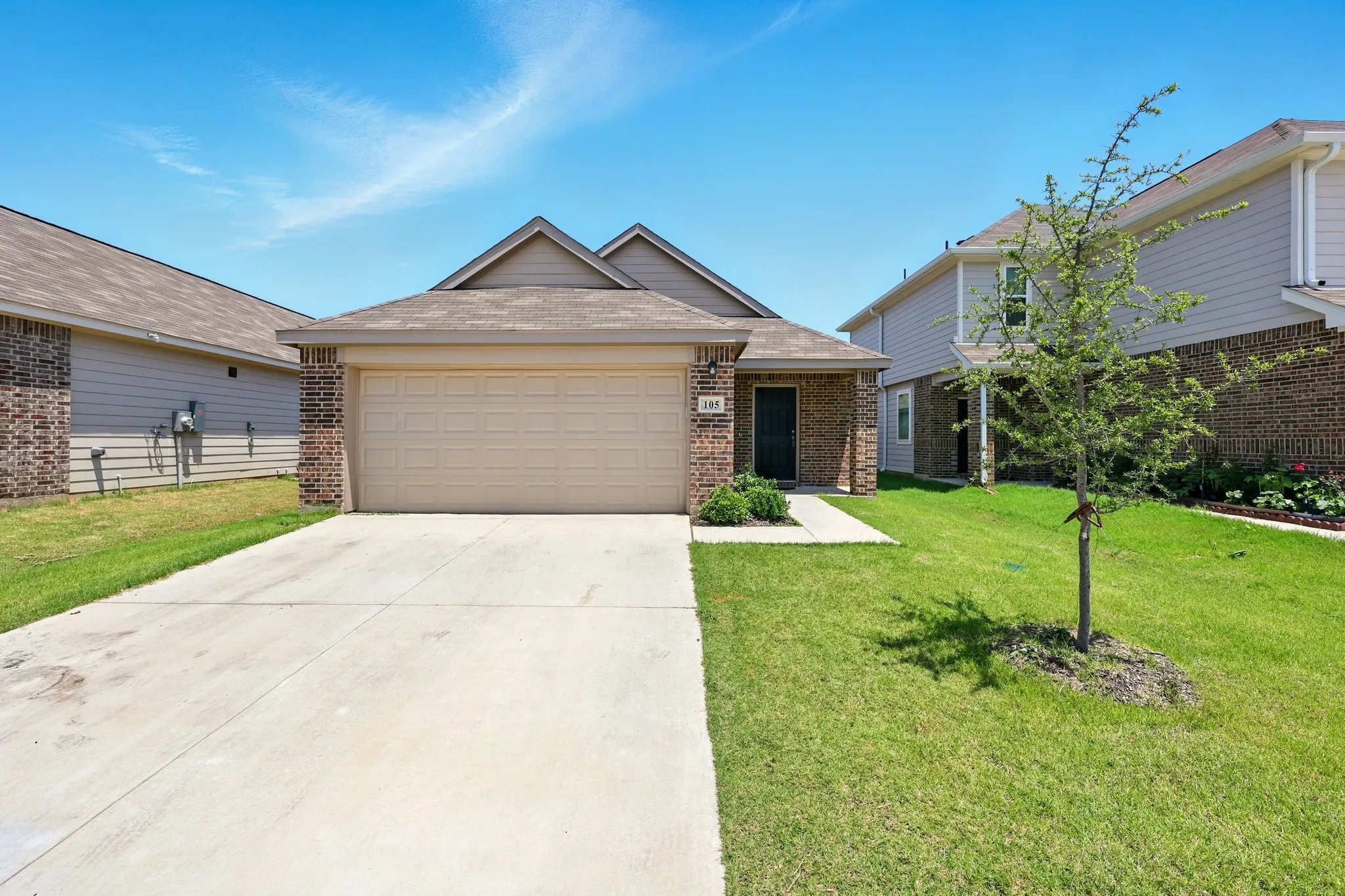Brick exterior with siding accents, attached garage, concrete driveway, and front lawn
