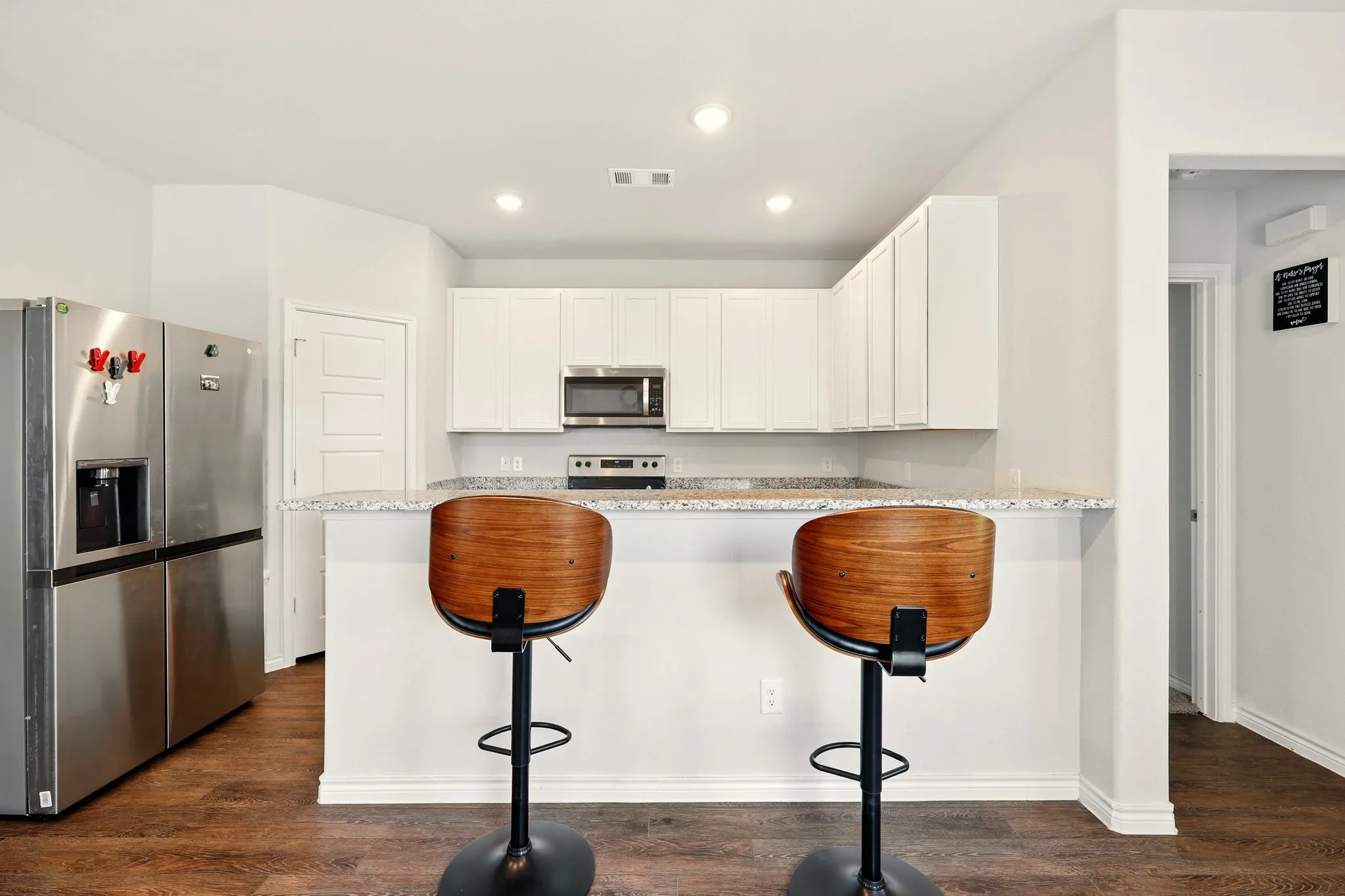 Kitchen featuring white cabinetry, stainless steel appliances, granite countertops, and wood-finish flooring