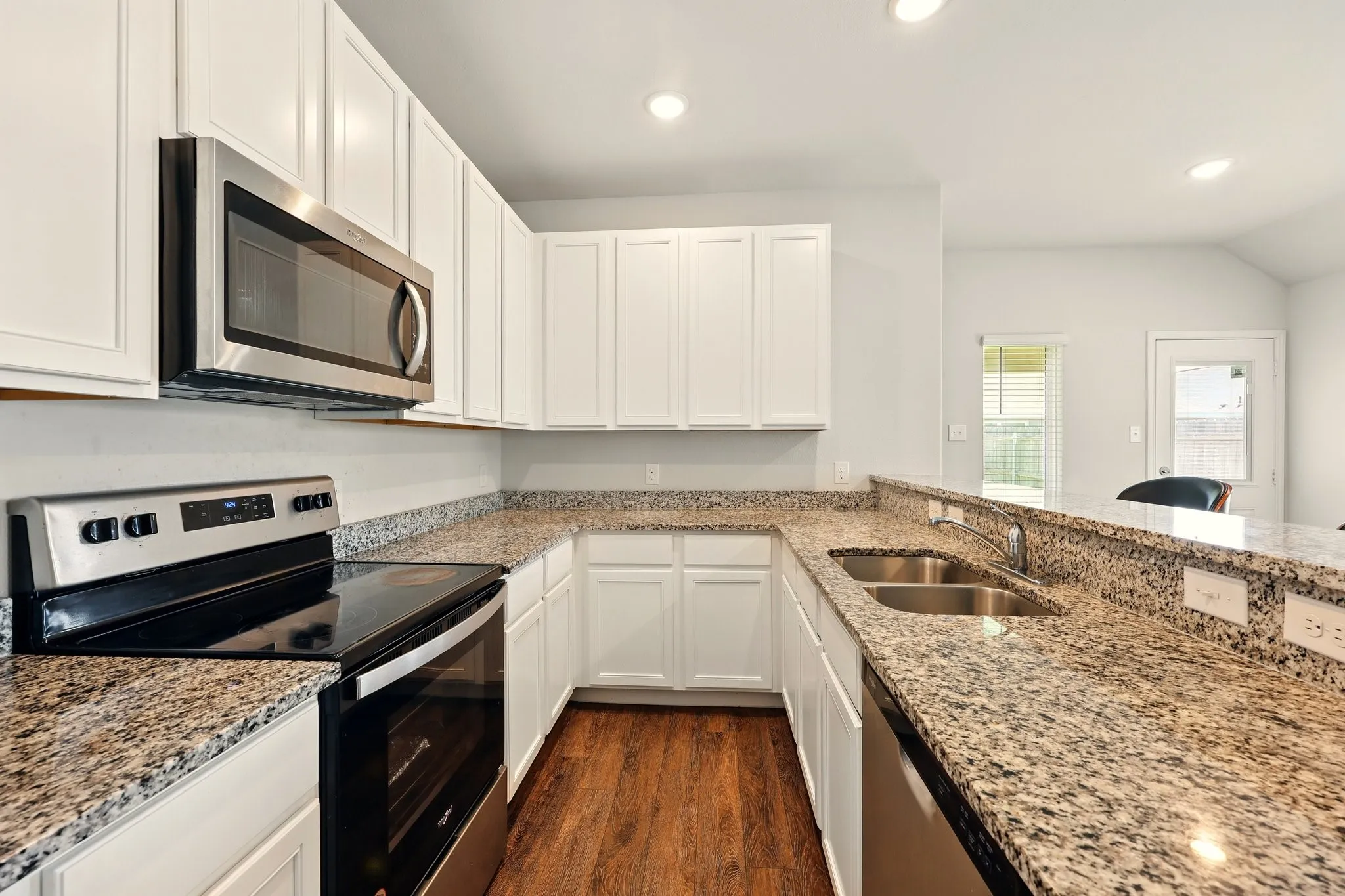 Kitchen featuring white cabinetry, granite countertops, stainless steel appliances, a double basin sink, and wood-finish flooring