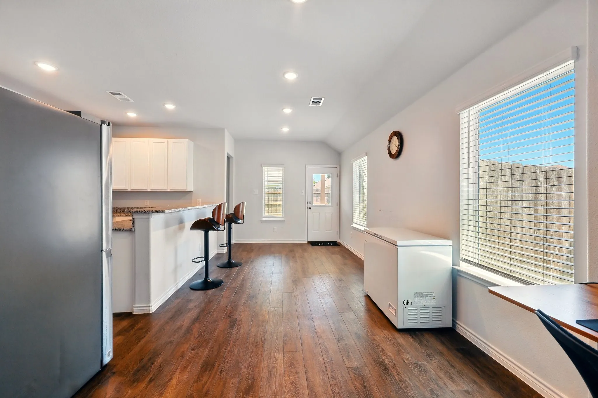 Open-concept living area featuring wood-finish flooring, recessed lighting, white cabinetry, a breakfast bar, and multiple windows