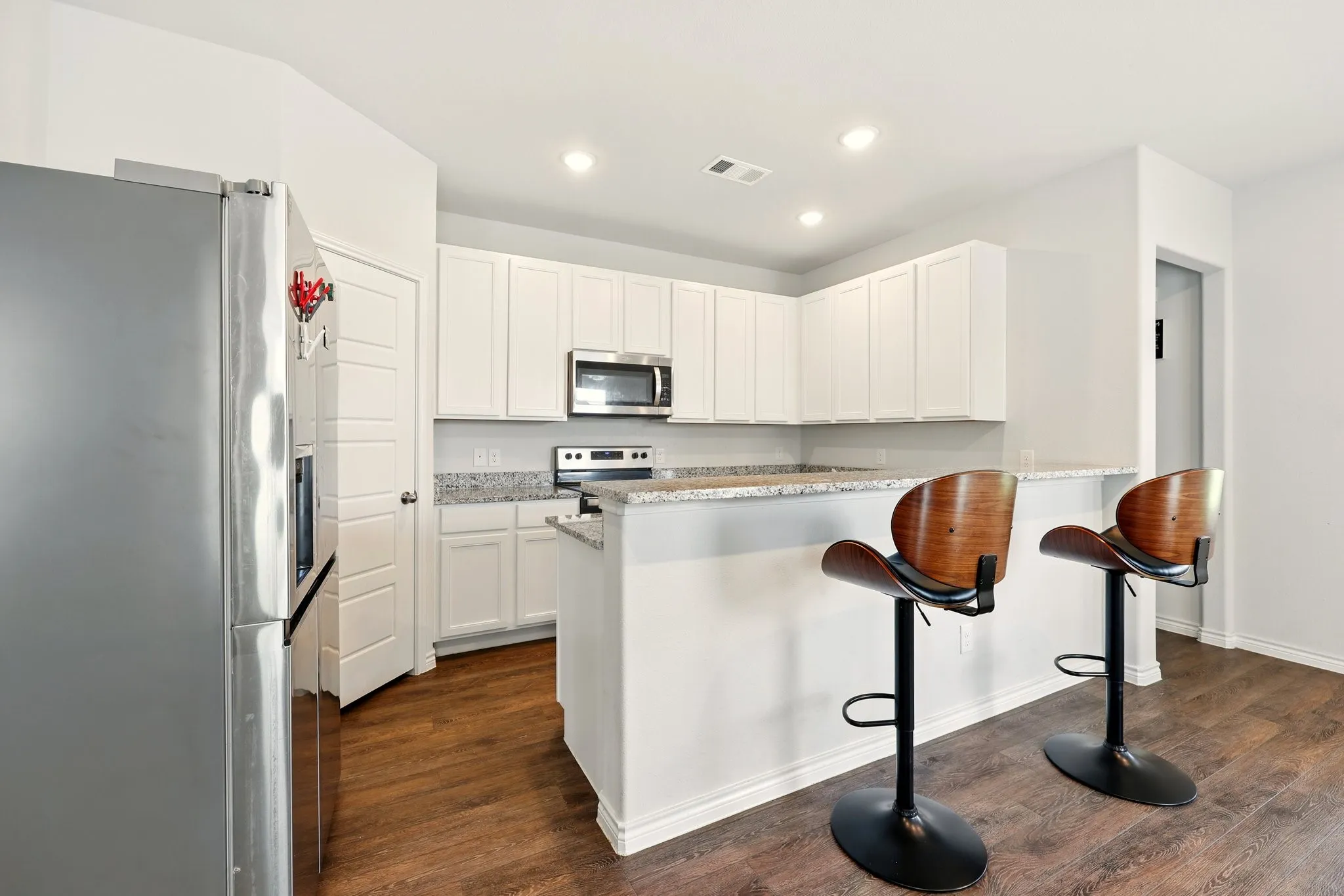 Kitchen featuring white cabinetry, granite countertops, stainless steel appliances, and wood-finish flooring