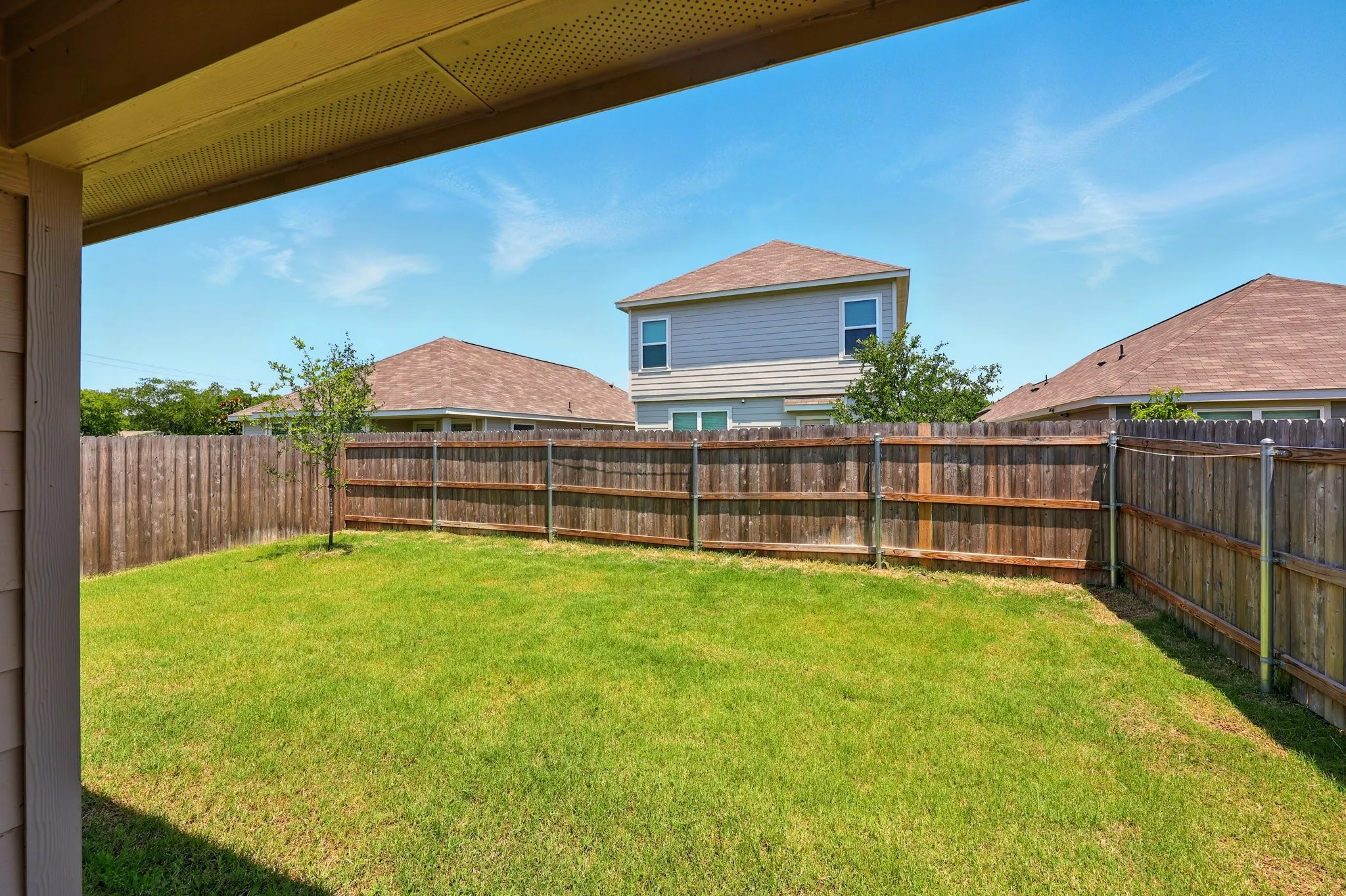 Expansive backyard featuring a green lawn, wood privacy fencing, and a young tree