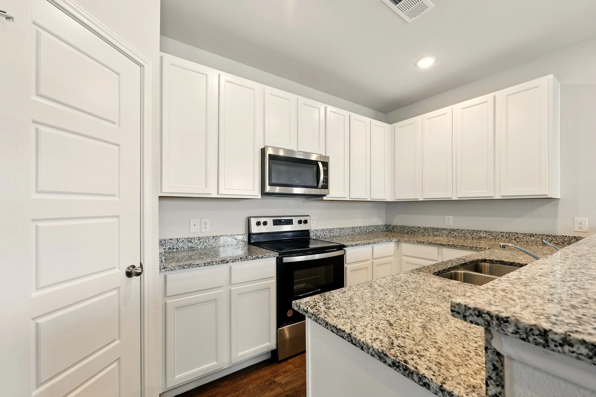 Modern kitchen featuring white cabinetry, granite countertops, stainless steel microwave, electric range, and a double basin sink