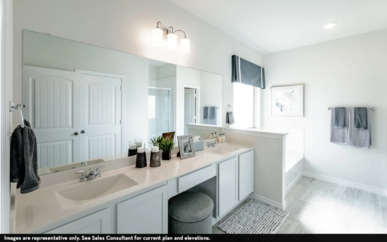 Dual vanity with integrated sinks and chrome fixtures, extensive wall-mounted mirror, built-in soaking tub, and tile flooring