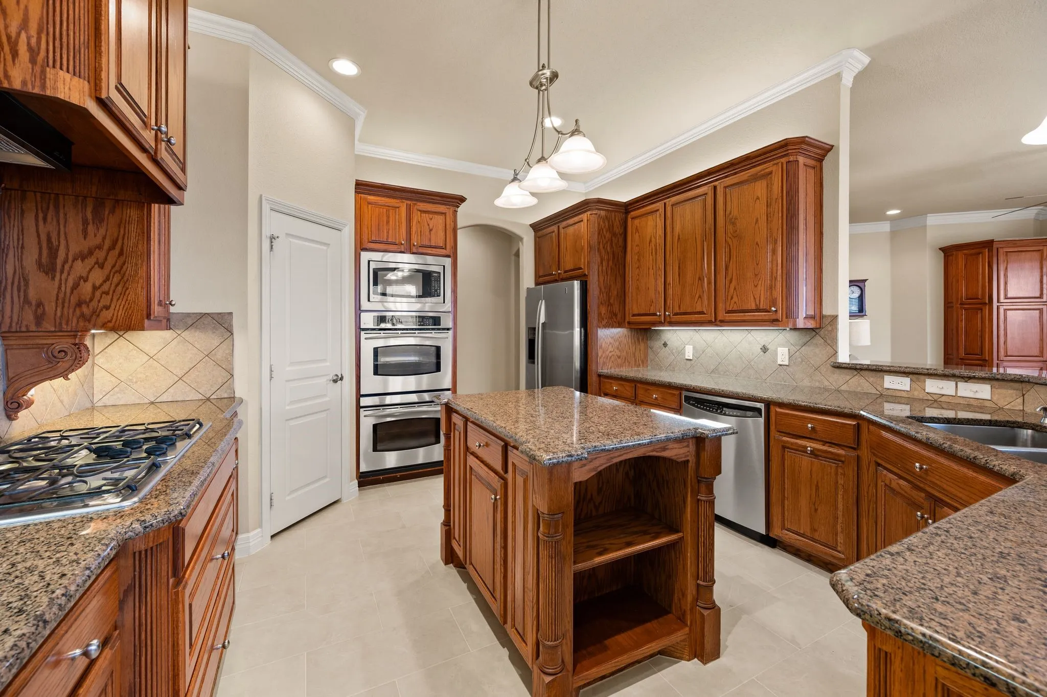 Kitchen featuring wood cabinetry, stone countertops, stainless steel double wall ovens, gas cooktop, and center island with built-in shelving