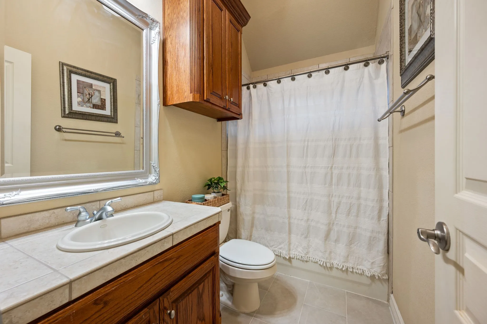 Bathroom featuring a tile-surround vanity with an integrated basin, stained wood cabinetry, a matching wall-mounted storage cabinet, and neutral tile flooring