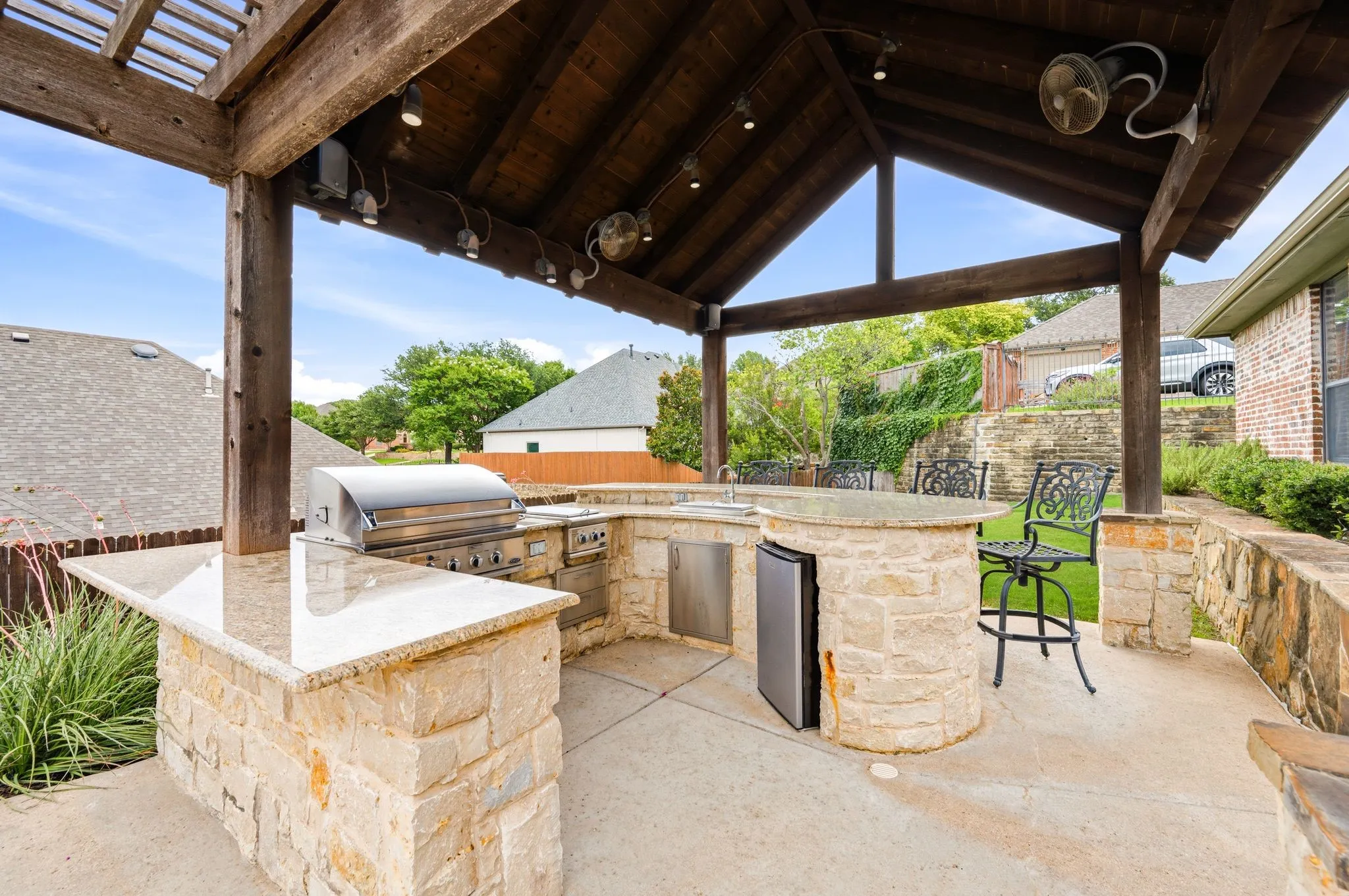 Covered outdoor kitchen featuring a built-in grill, integrated sink, and under-counter refrigerator