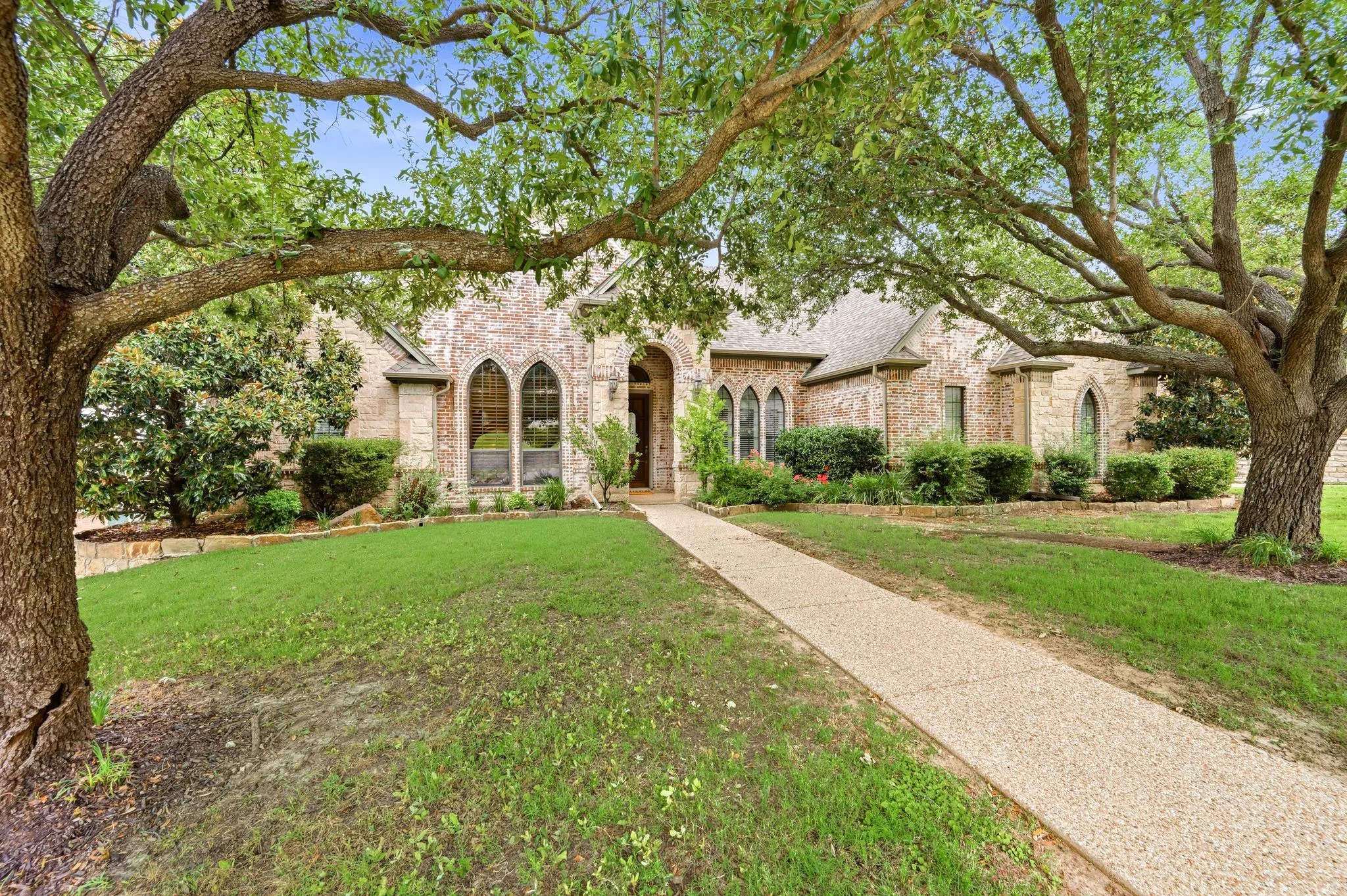 Brick and stone facade with arched windows, mature trees, and a textured pathway
