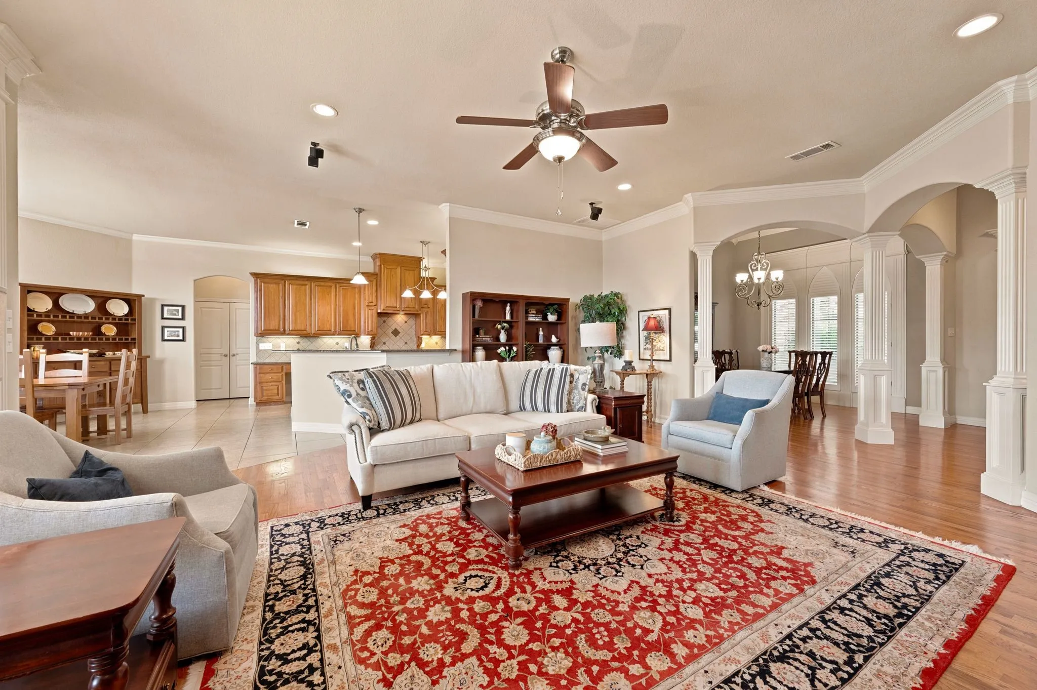 Open-concept living space featuring wood-finish flooring, recessed lighting, a ceiling fan, and architectural columns defining the entryway