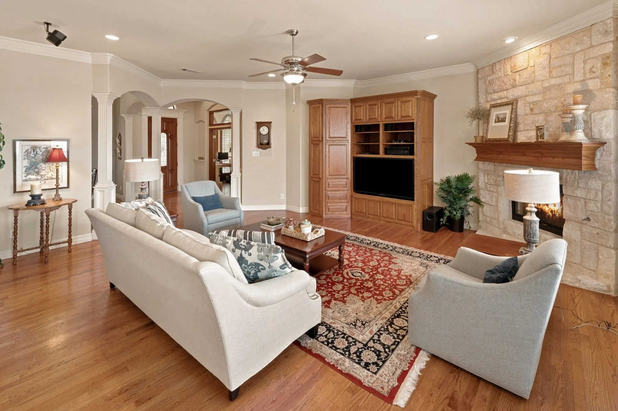 Living space featuring wood-finish flooring, a stone-clad fireplace with a substantial wood mantel, and built-in entertainment cabinetry