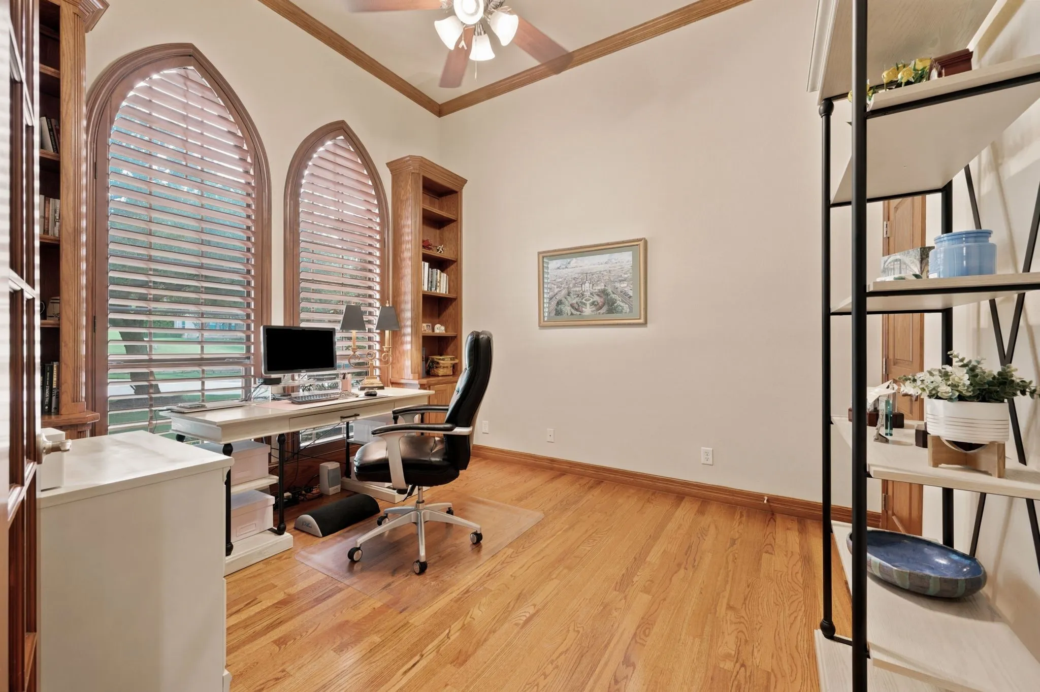 Spacious room featuring arched windows with wood frames and slatted blinds, hardwood flooring, and a ceiling fan