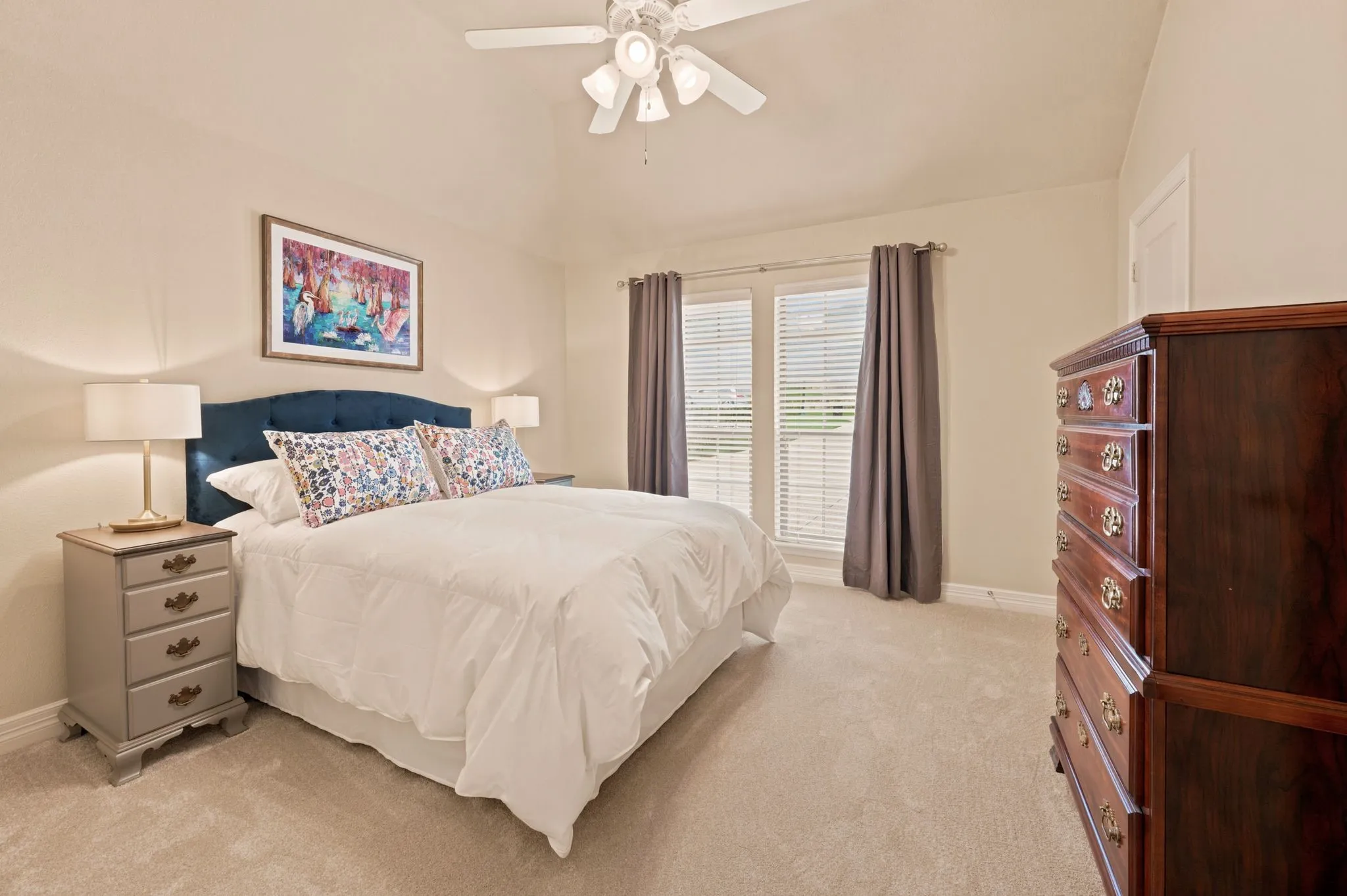 Vaulted ceiling bedroom with a ceiling fan, plush carpet flooring, and two large windows with blinds