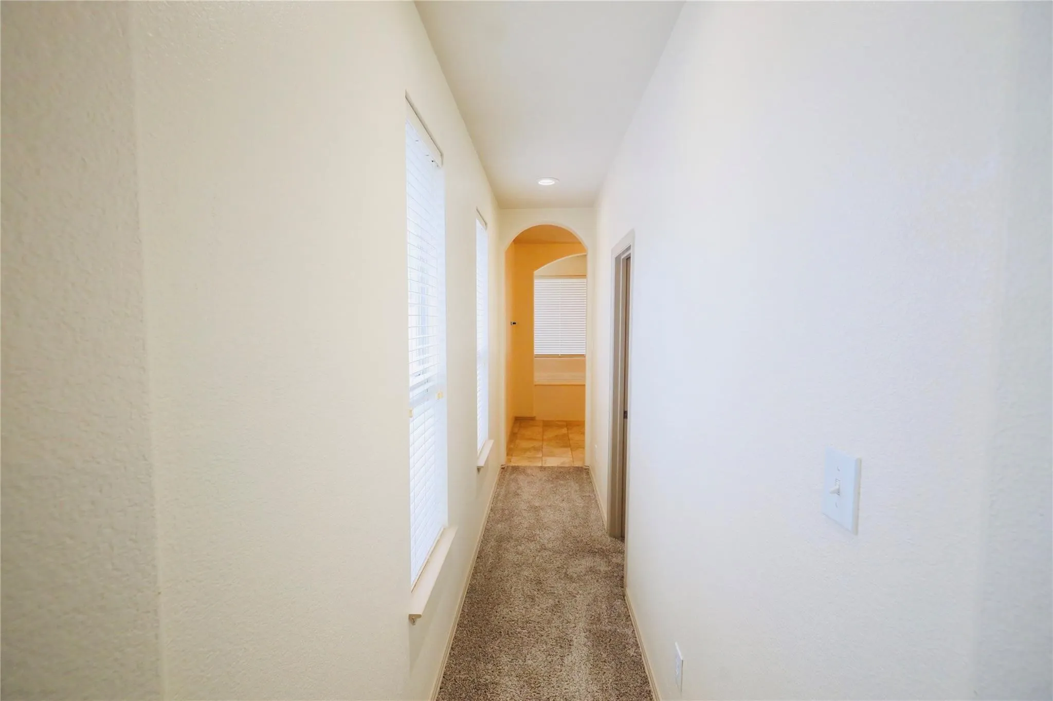 Hallway featuring carpet flooring, multiple windows with blinds, and an arched entryway