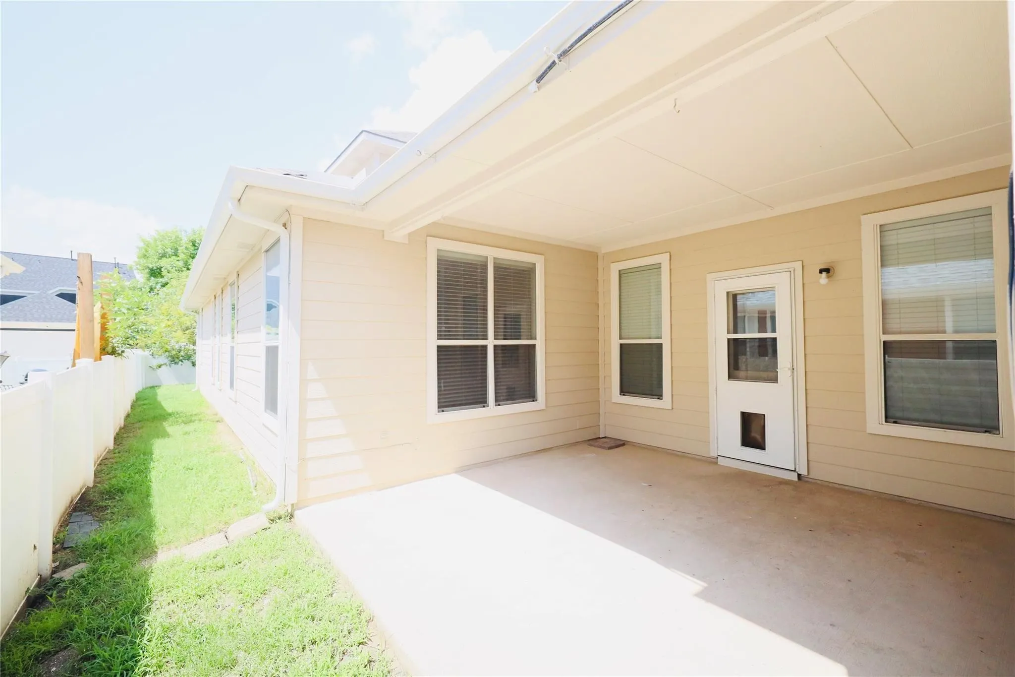 Covered patio with concrete flooring, framed by multiple windows and a white exterior door