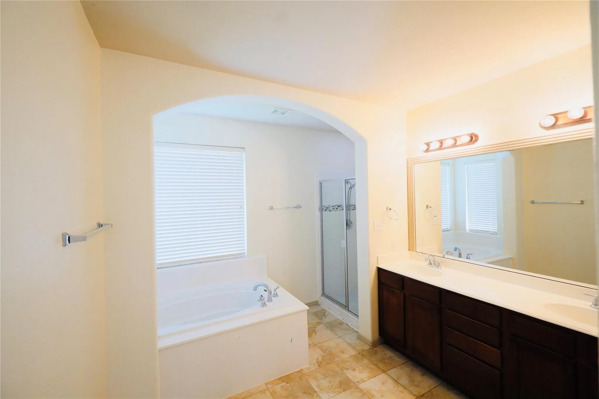 Arched doorway leading to a tiled shower, built-in bathtub, and window with horizontal blinds