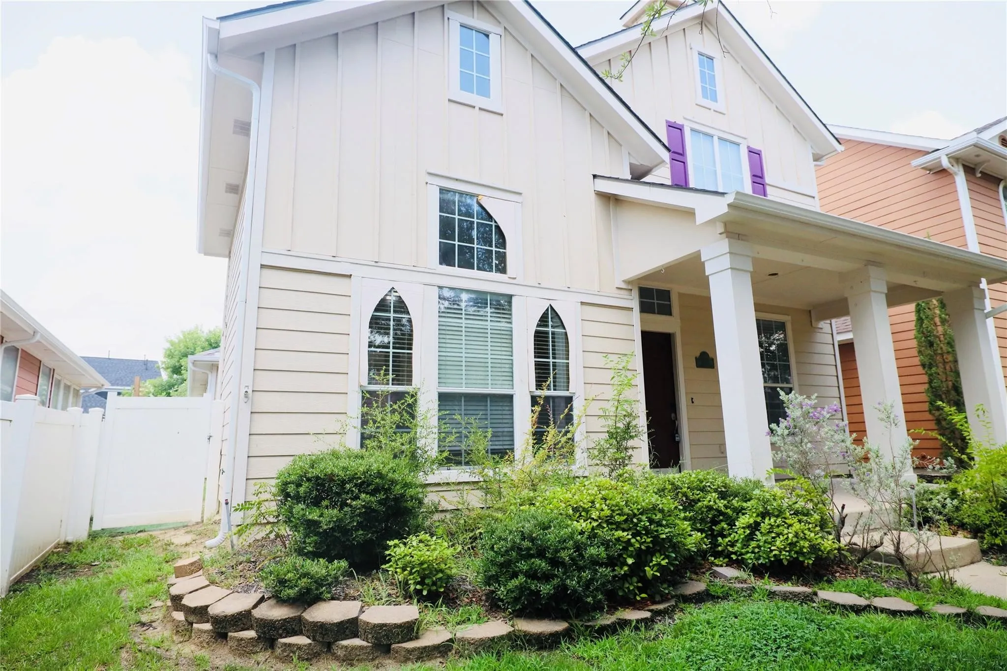 Cream-colored siding exterior with board and batten accents, arched windows, covered porch with columns, and mature landscaping