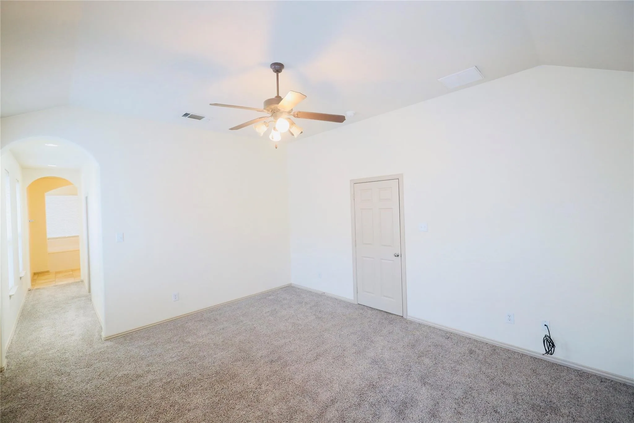 Vaulted ceiling with ceiling fan, light-toned carpeting, arched entryway, and paneled interior door