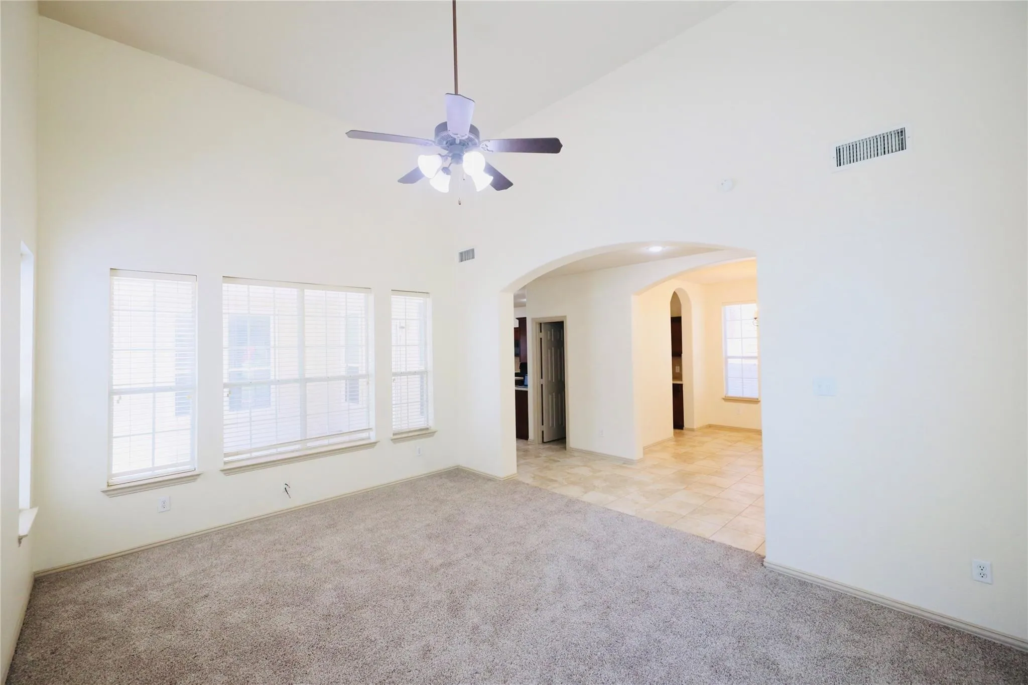 Vaulted ceiling, ceiling fan, multiple windows with blinds, arched doorway, and carpet flooring