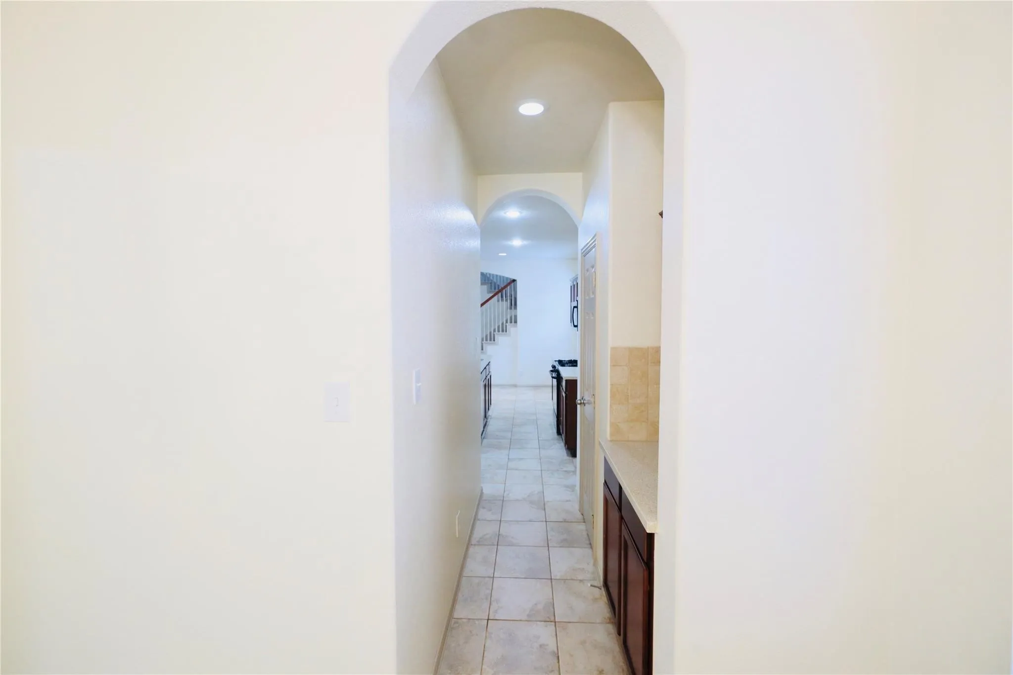 Arched hallway entrance with recessed lighting, tile flooring, and dark wood-finish cabinetry