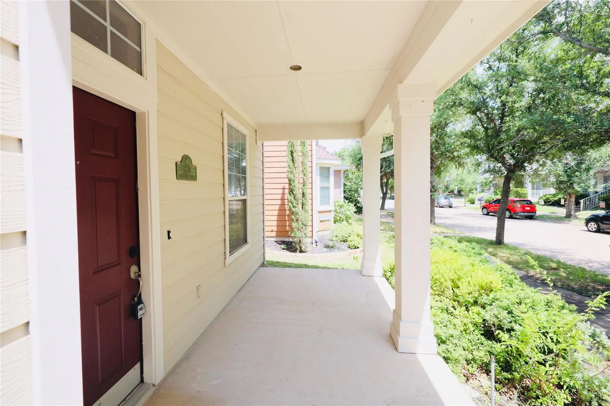 Inviting covered porch with a red paneled entry door, transom window, and classic white columns