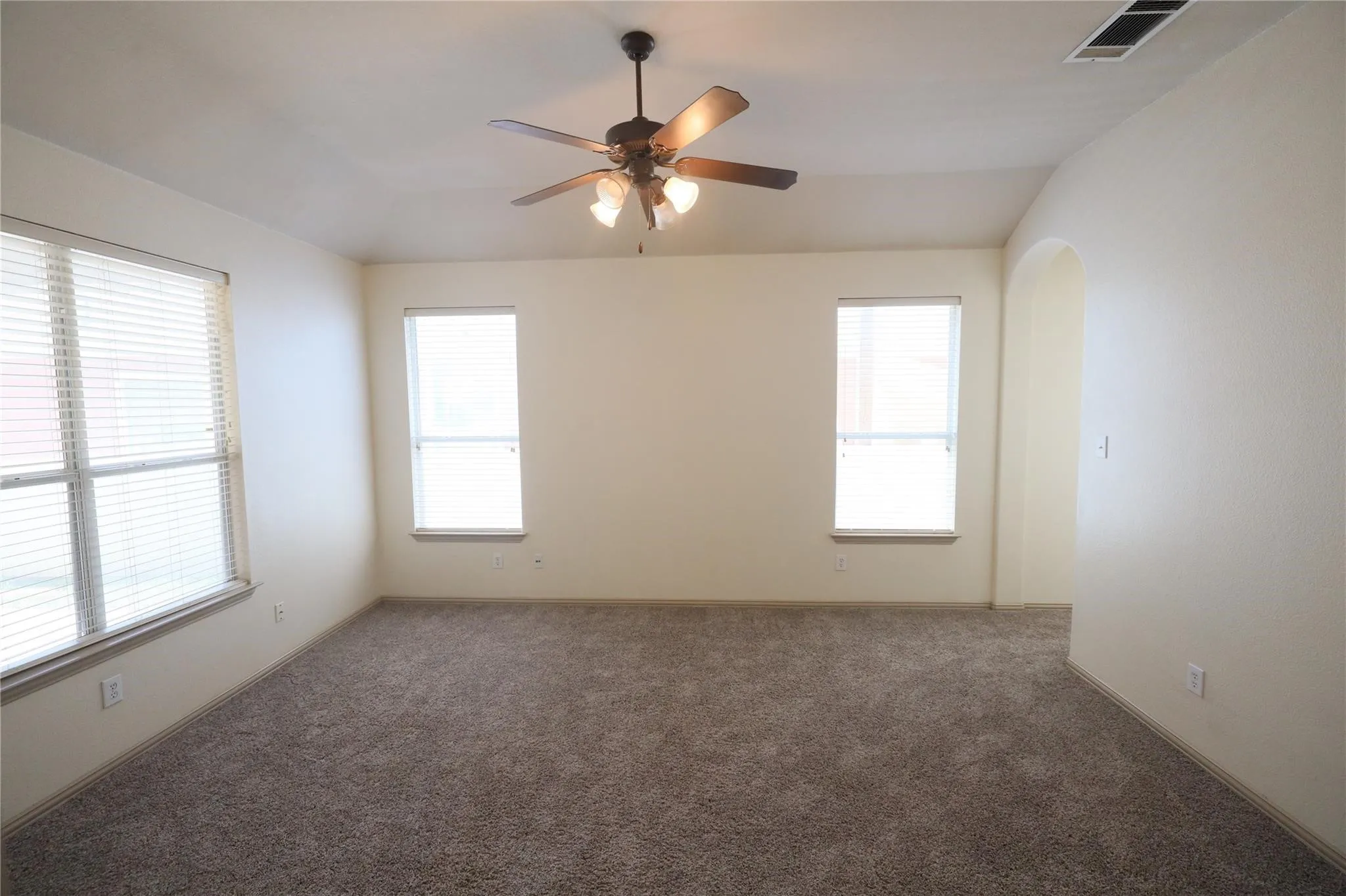 Carpeted room featuring multiple windows with blinds, a ceiling fan with integrated lighting, and an arched entryway