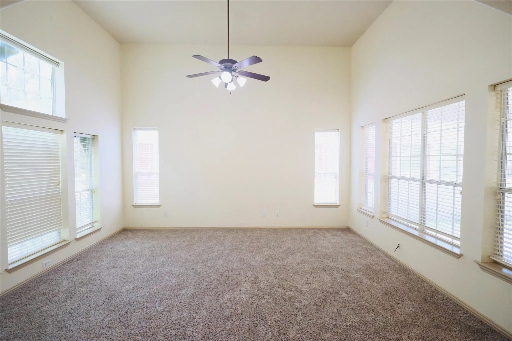 Vaulted ceilings, a ceiling fan with integrated lighting, multiple large windows, and neutral carpeting