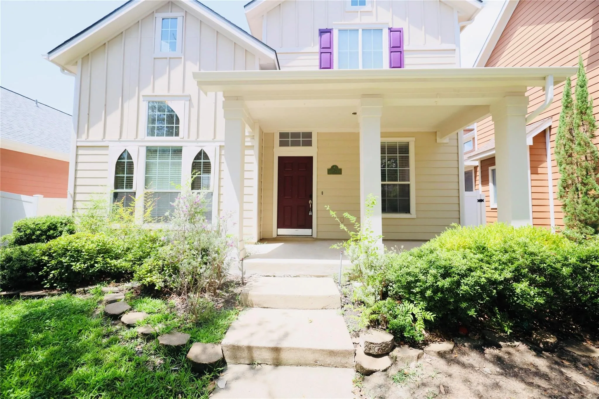 Exterior featuring a covered porch, contrasting entry door, window shutters, and a walkway with stone steps