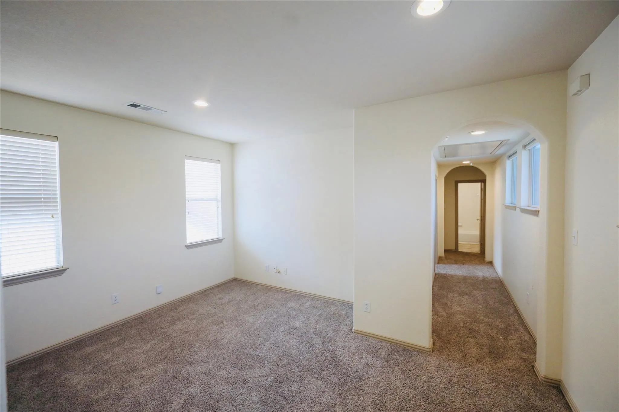 Recessed ceiling lighting, arched entryway, and neutral carpeting