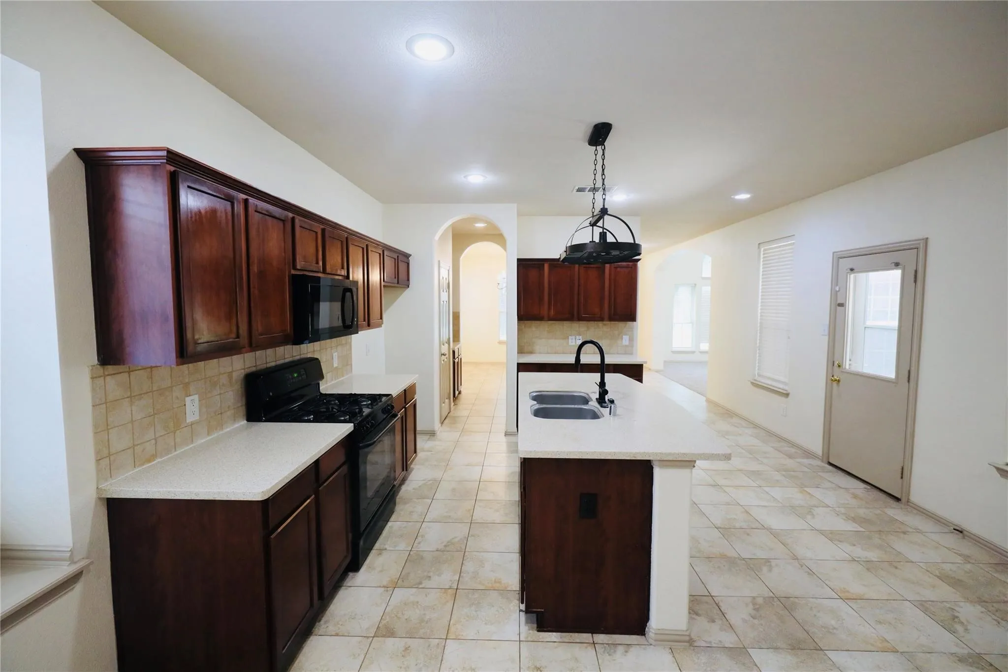 Kitchen featuring dark wood cabinetry, light-toned countertops, a tile backsplash, and a central island with a double basin sink