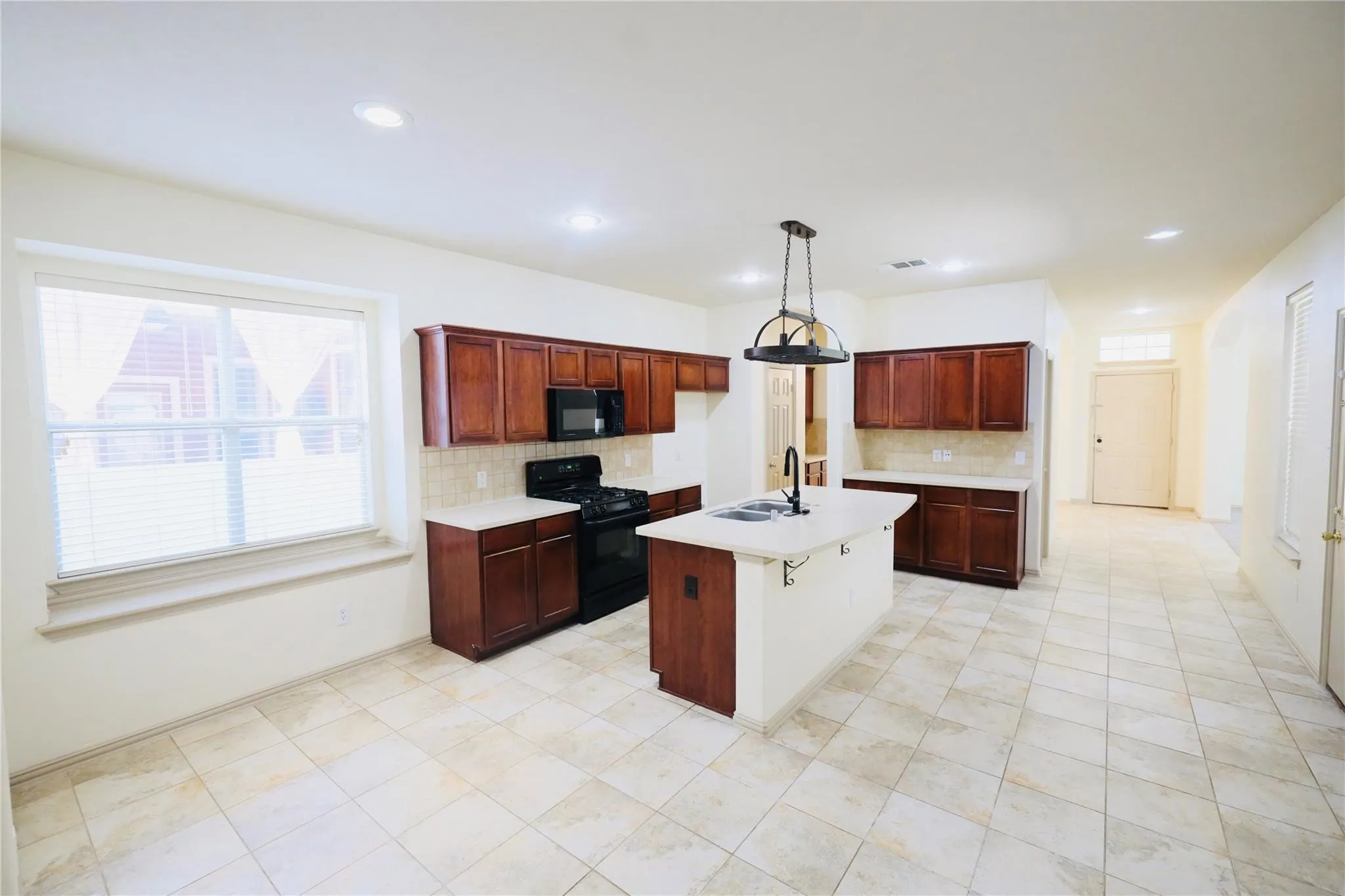 Kitchen featuring recessed lighting, a central island with a pendant light, rich wood-finish cabinetry, a tiled backsplash, and stone-look tile flooring
