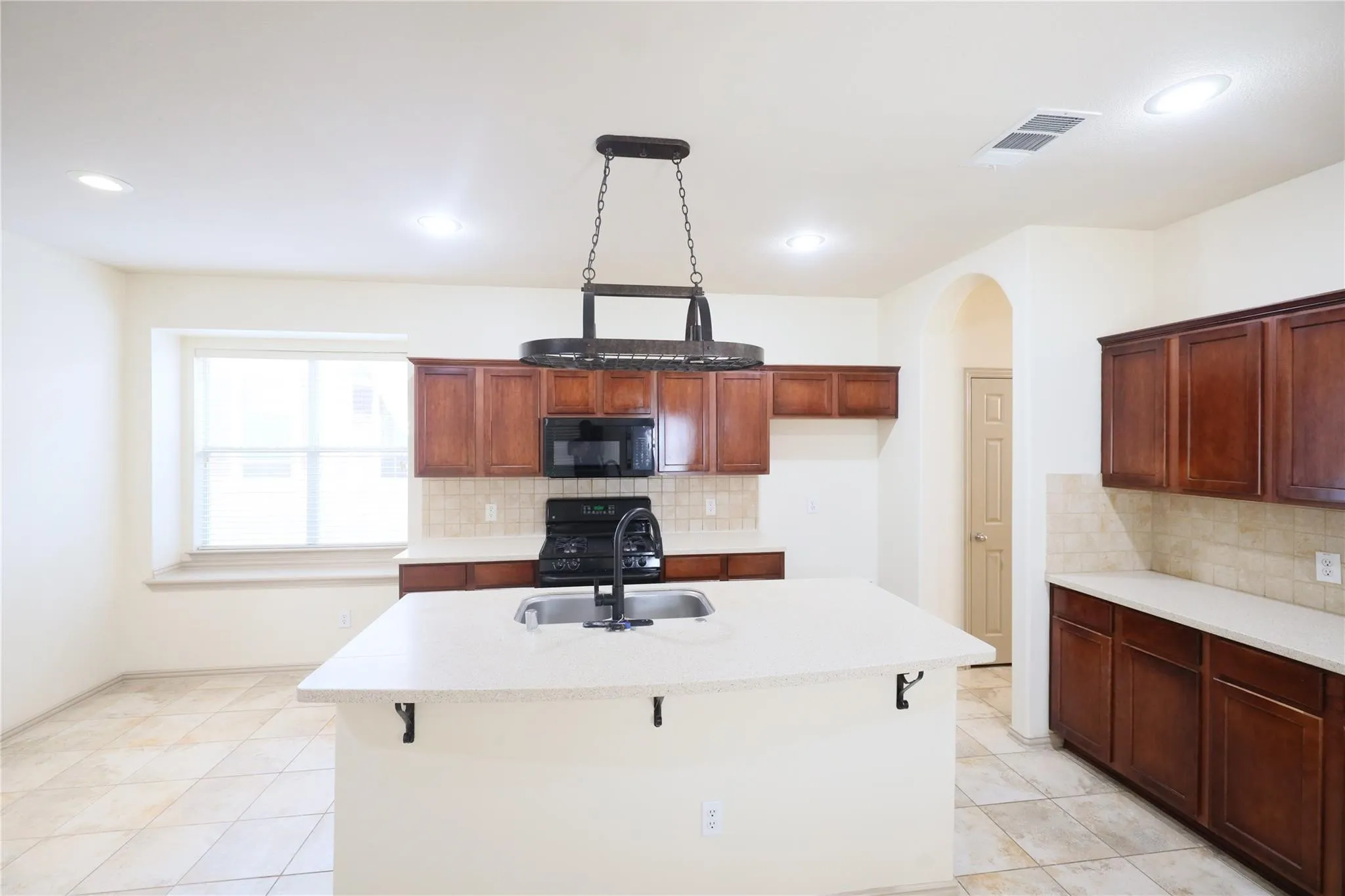 Spacious kitchen featuring an island with an integrated sink, dark wood cabinetry, light countertops, and tile flooring