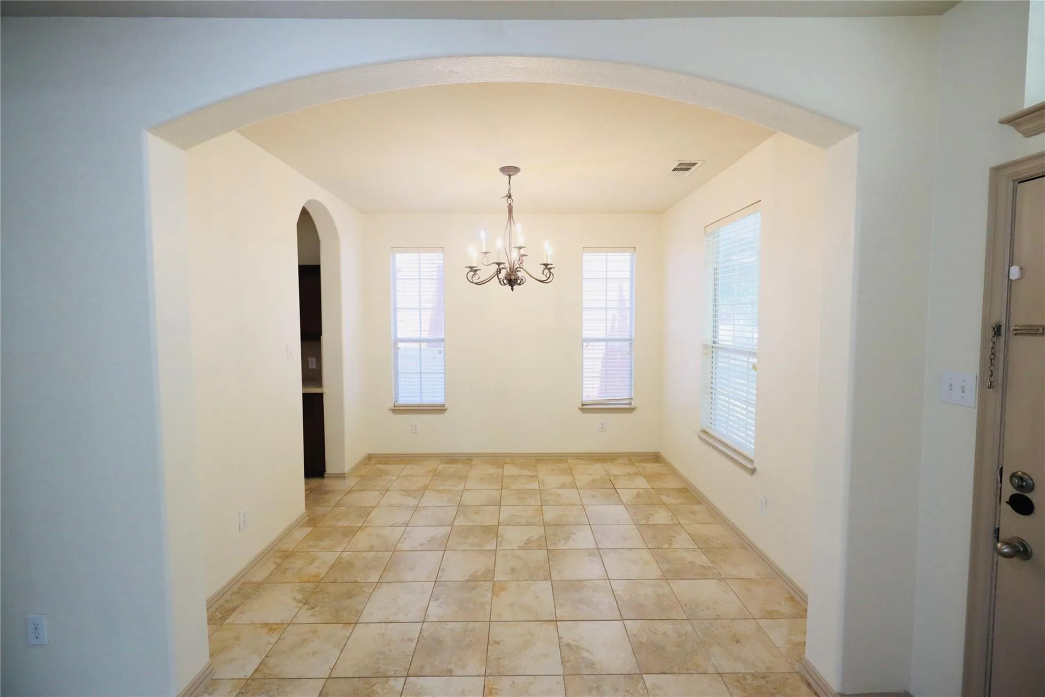 Arched entryway opening to a room featuring tiled flooring, multiple windows with blinds, and a decorative chandelier