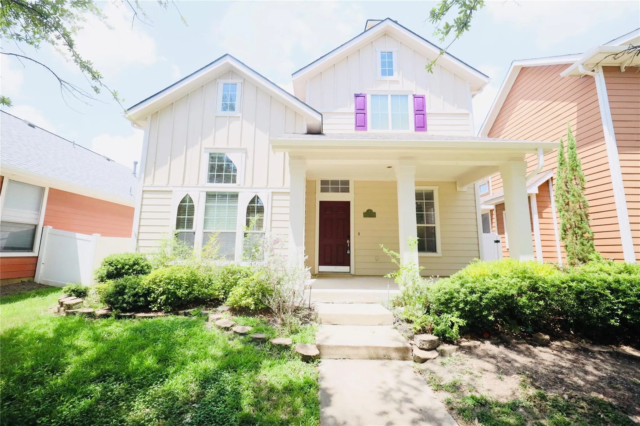 Two-story residence featuring a covered front porch, decorative purple shutters, a red entry door, and varied window styles