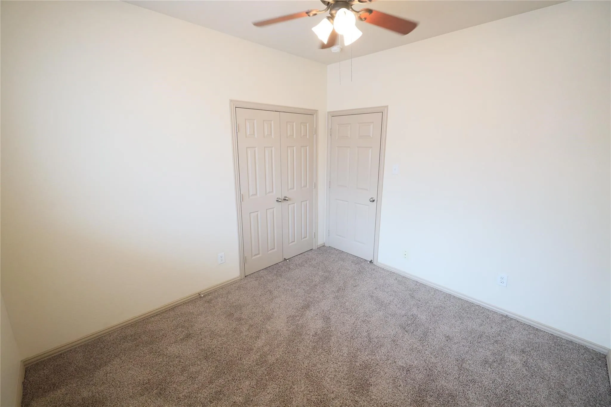 Soft neutral wall color, textured carpet, ceiling fan with integrated lighting, paneled bi-fold closet doors, and a paneled single door