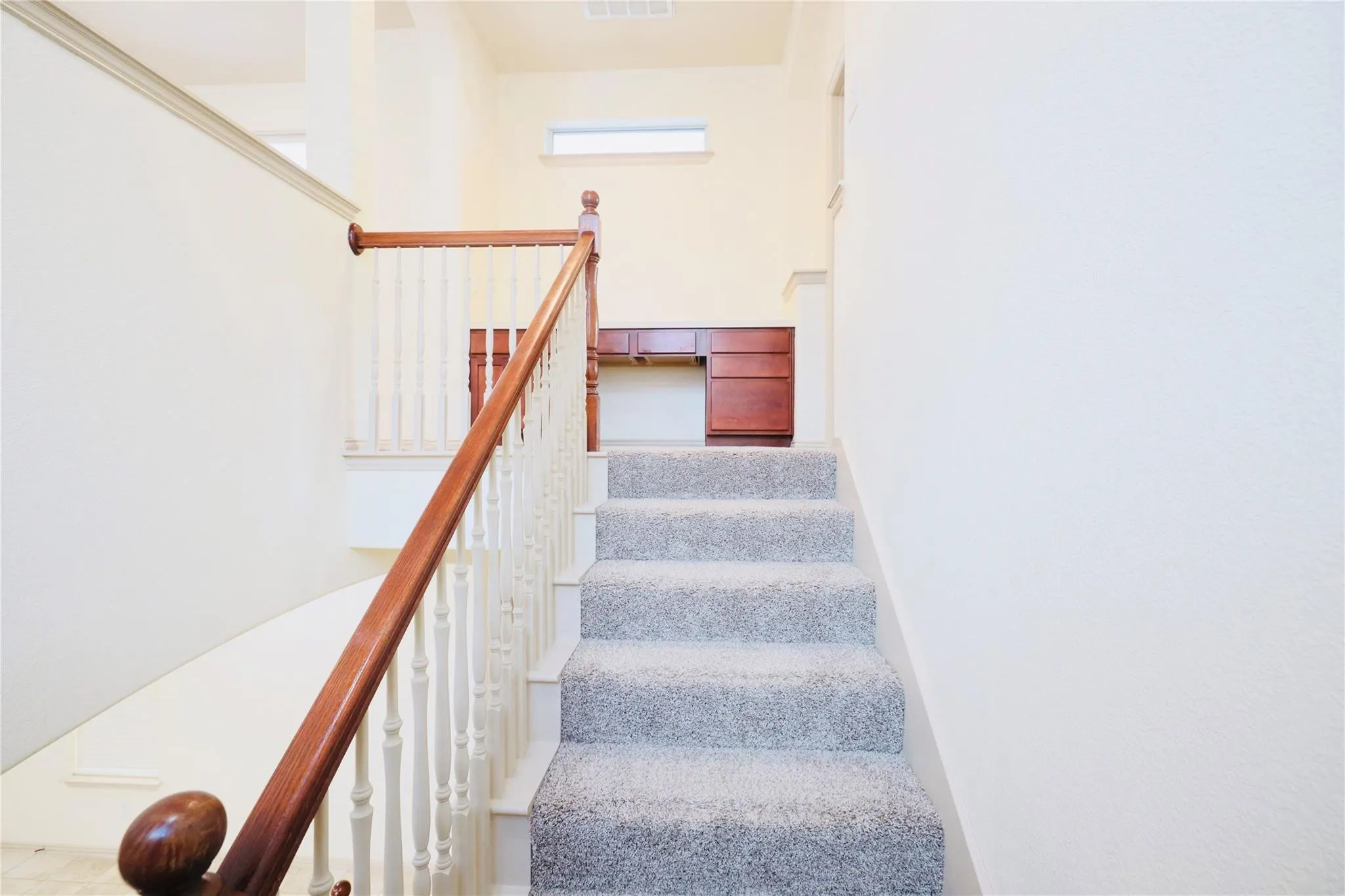 Carpeted staircase featuring a wood handrail and painted balusters