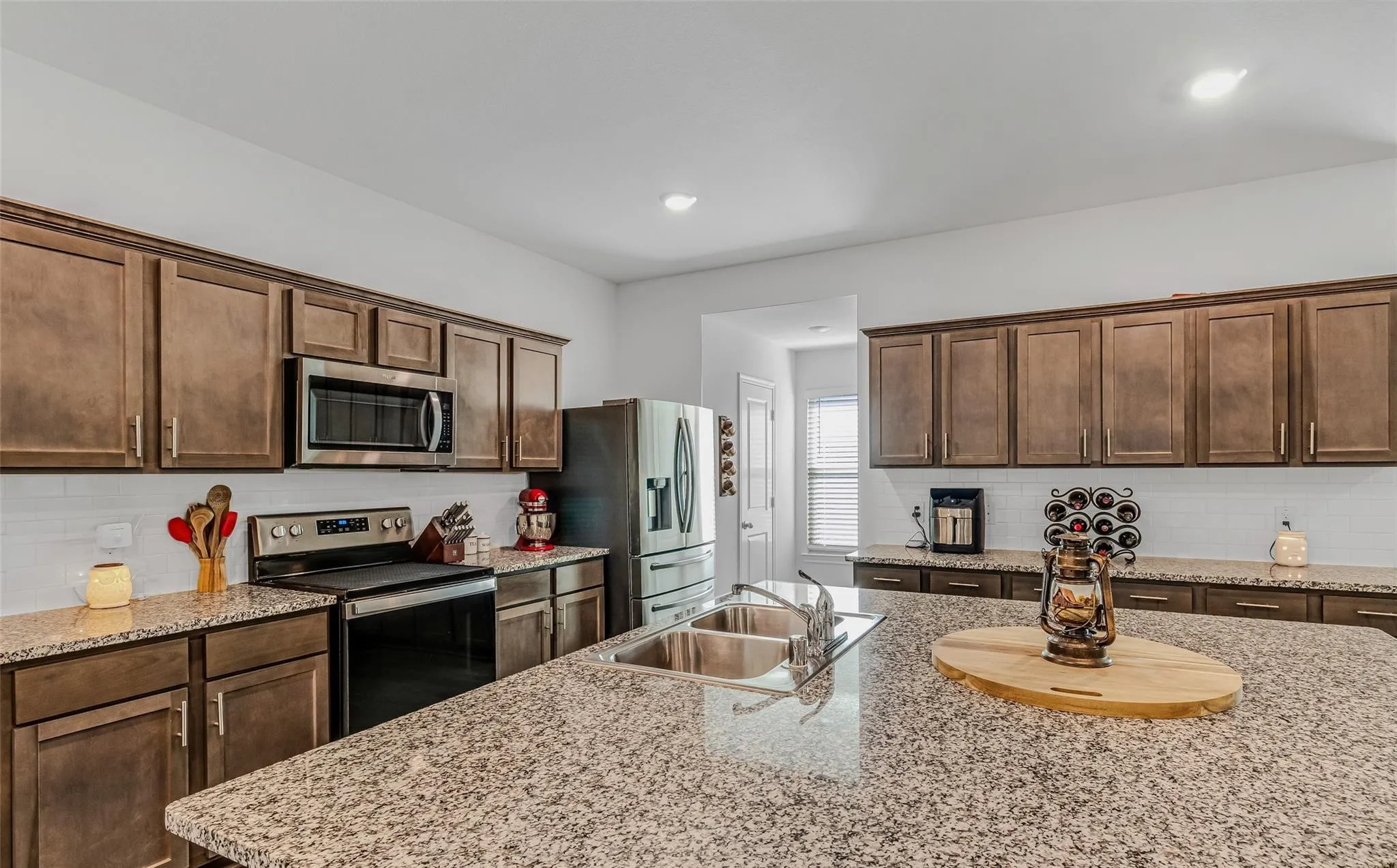 Kitchen with decorative backsplash, stainless steel appliances, dark brown cabinets, sink, and light stone counters