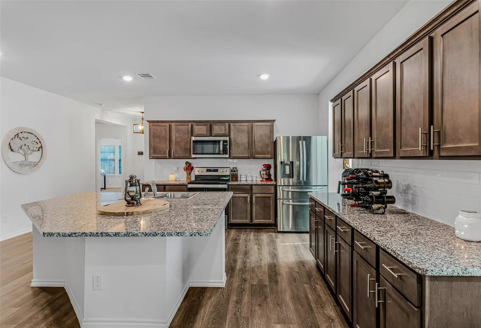Kitchen with dark brown cabinets, an island with sink, dark hardwood / wood-style flooring, light stone countertops, and stainless steel appliances
