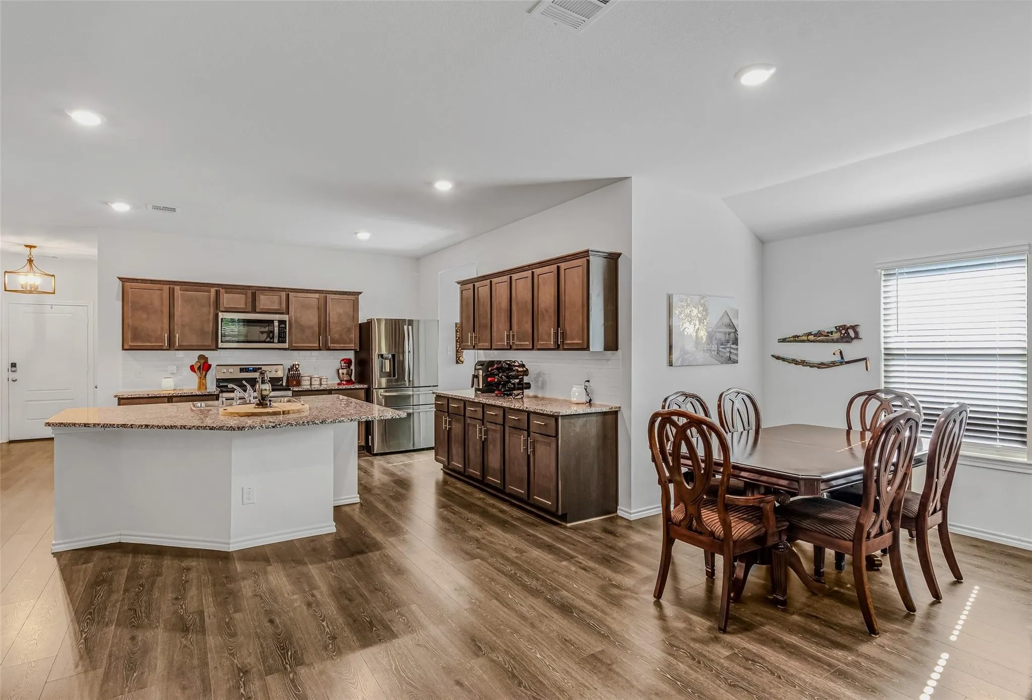 Kitchen with lofted ceiling, a kitchen island with sink, dark hardwood / wood-style floors, appliances with stainless steel finishes, and light stone counters