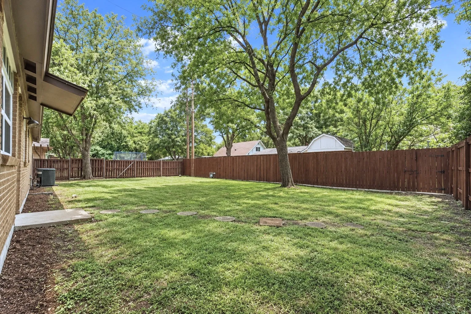 Large private backyard with grass, shade tree, sprinkler system, full fence