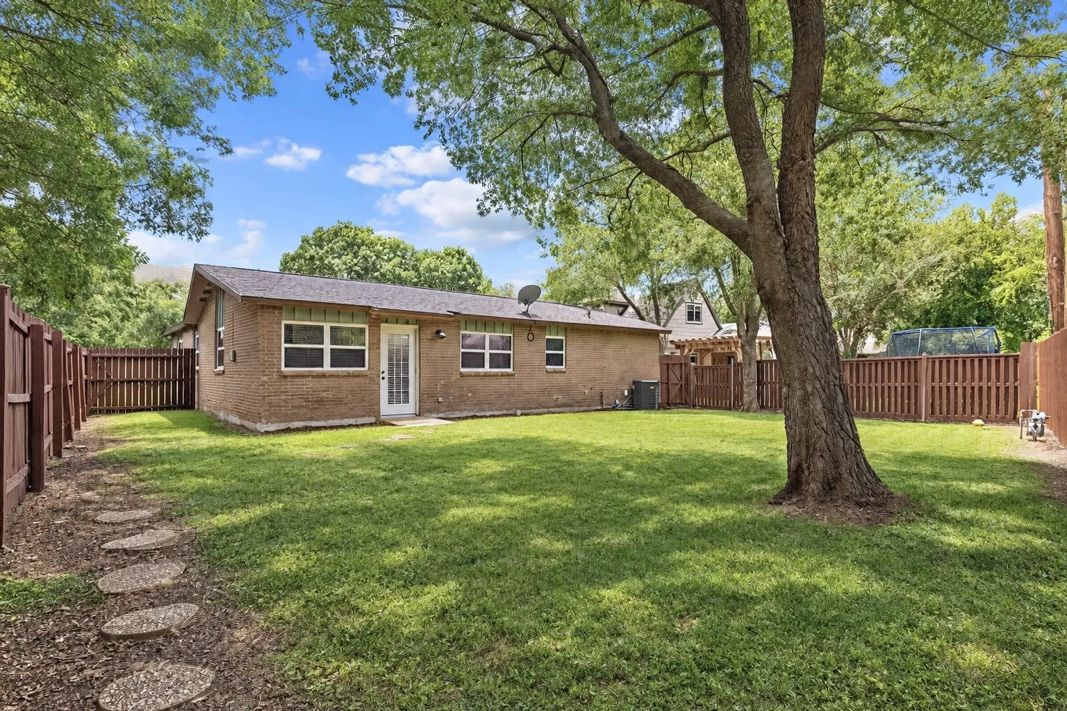 Large private backyard with grass, shade tree, sprinkler system, full fence