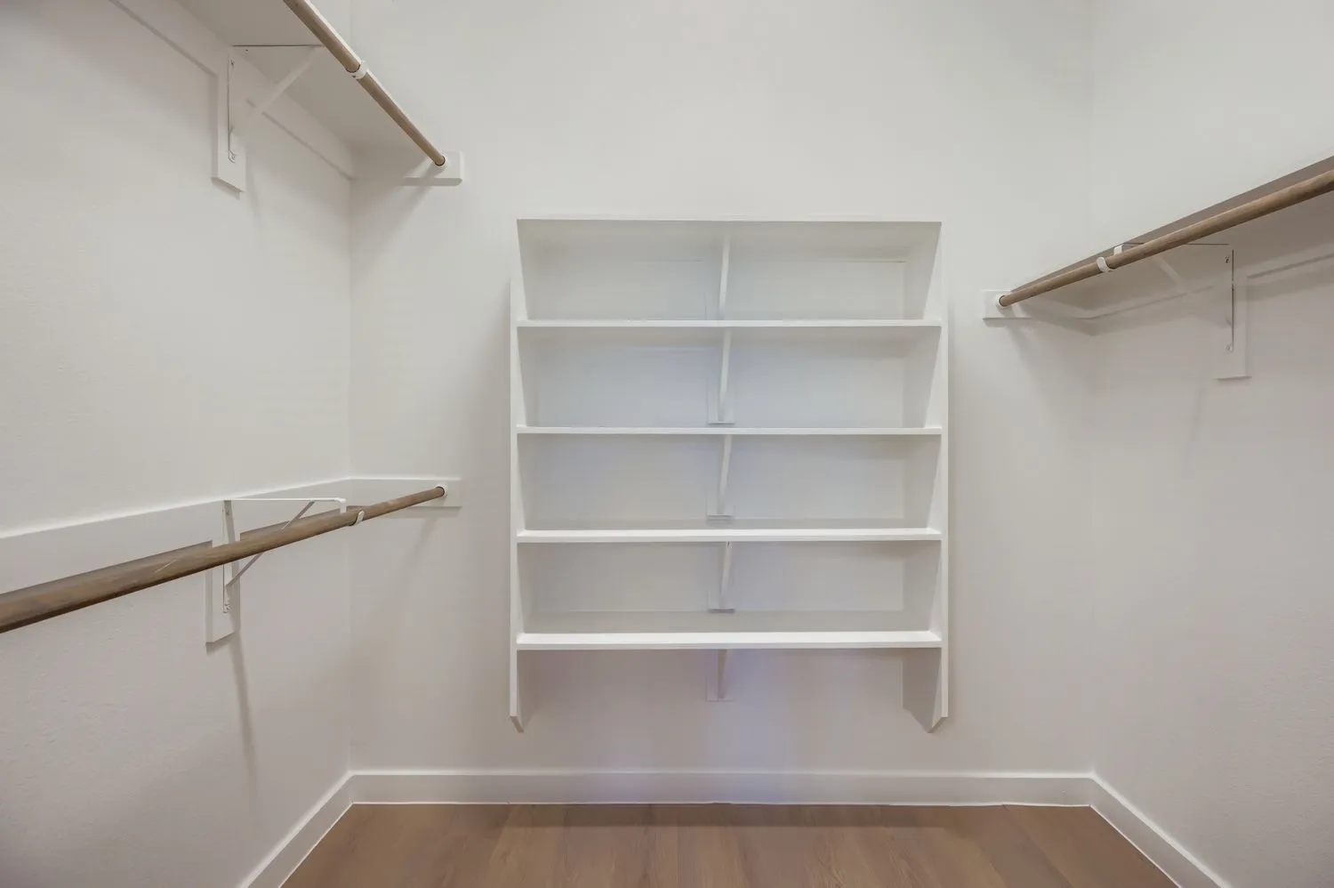 Storage area featuring custom white built-in shelving, wood-finish hanging rods, and wood-finish flooring
